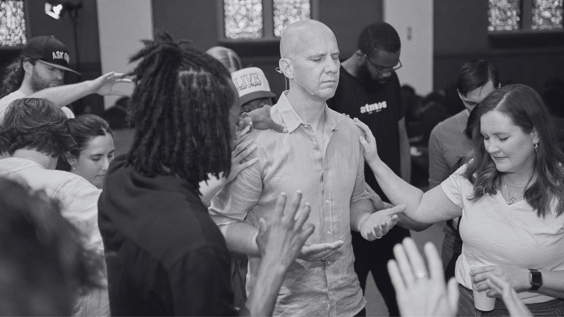 A group of people praying with their eyes closed, heads bowed, and hands raised or resting on others before a Grace Capital City church worship service in Washington, DC.