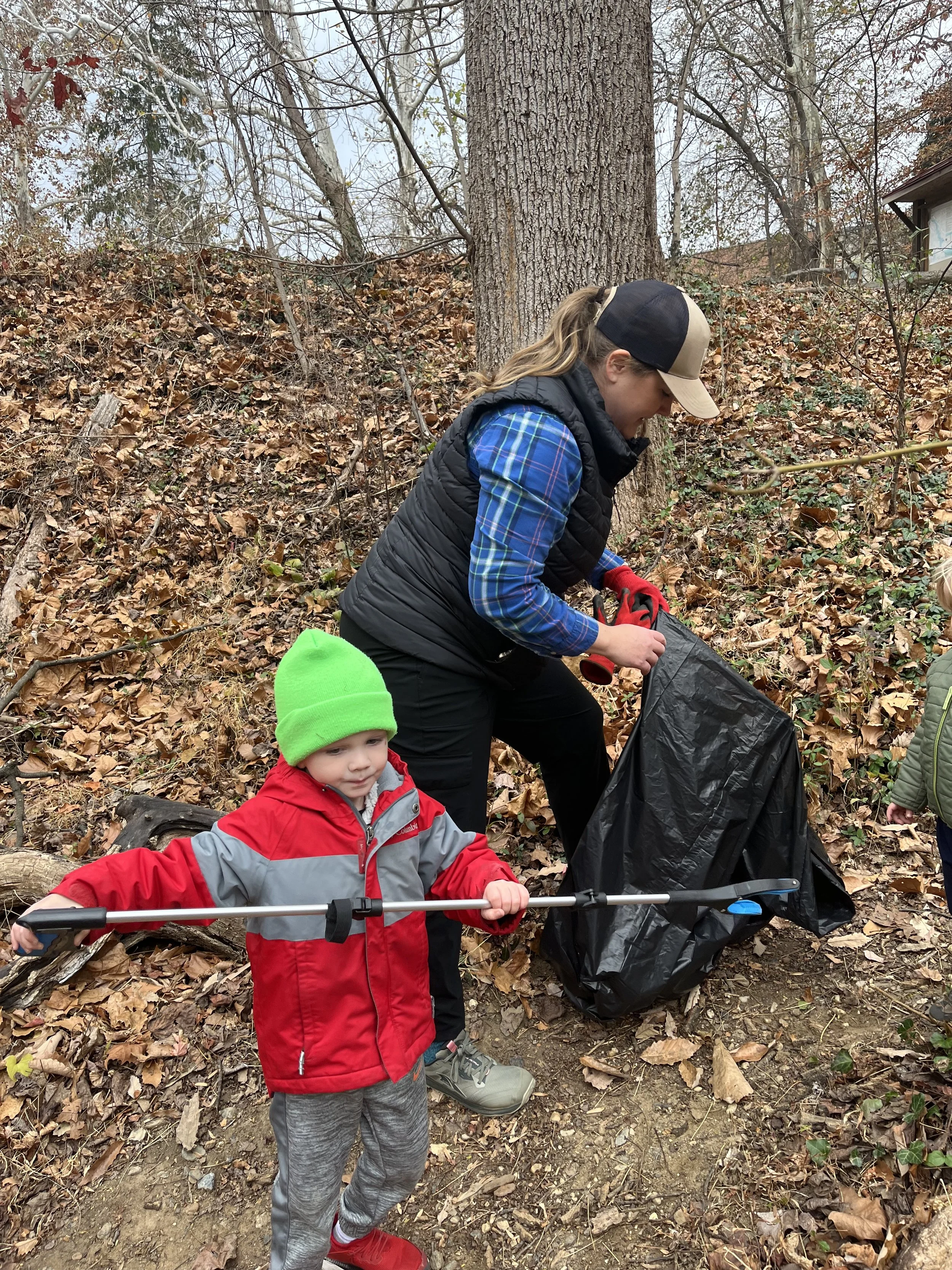 A woman and child collect fallen leaves and debris in a wooded area and place into a trash bag during a community service opportunity with Grace Capital City, a church in Washington, DC.
