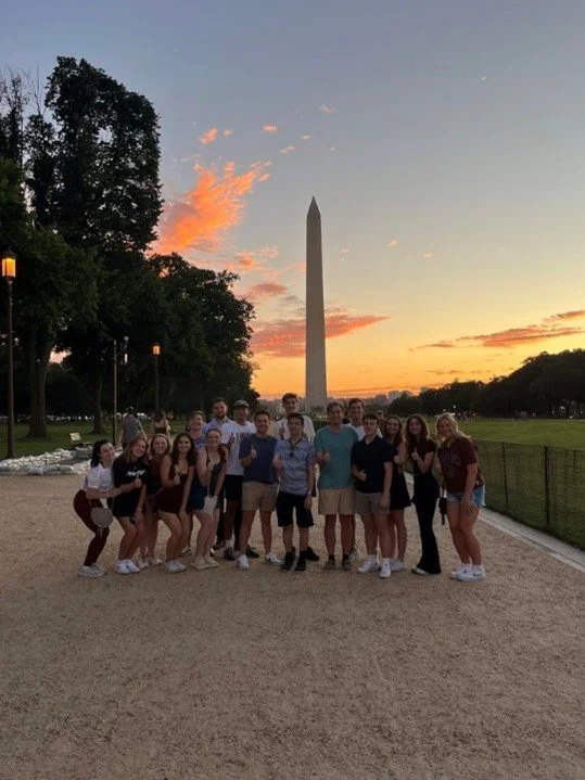 Group of young people posing in front of the Washington Monument during sunset.
