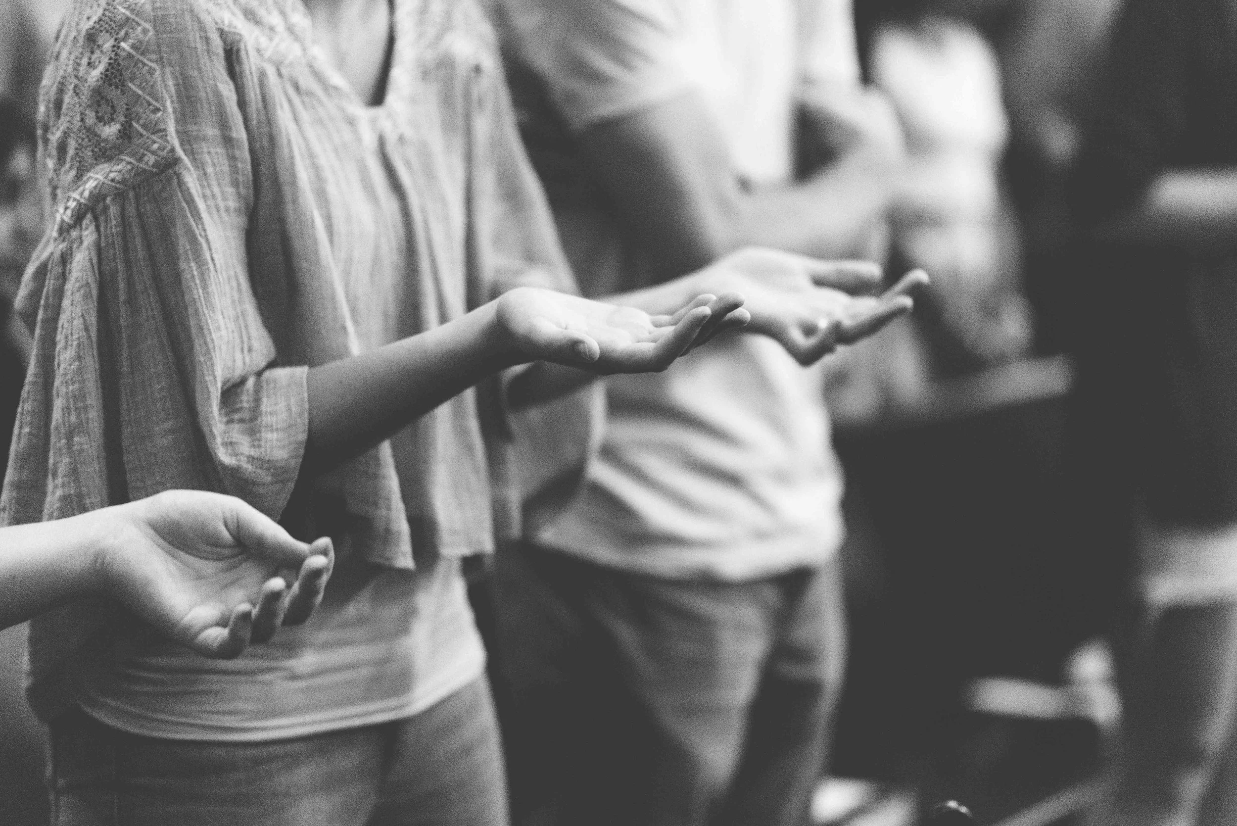 A black and white photo of a group of people standing in a line with open hands, worshipping and praying during a Grace Capital City church worship service in Washington, DC.