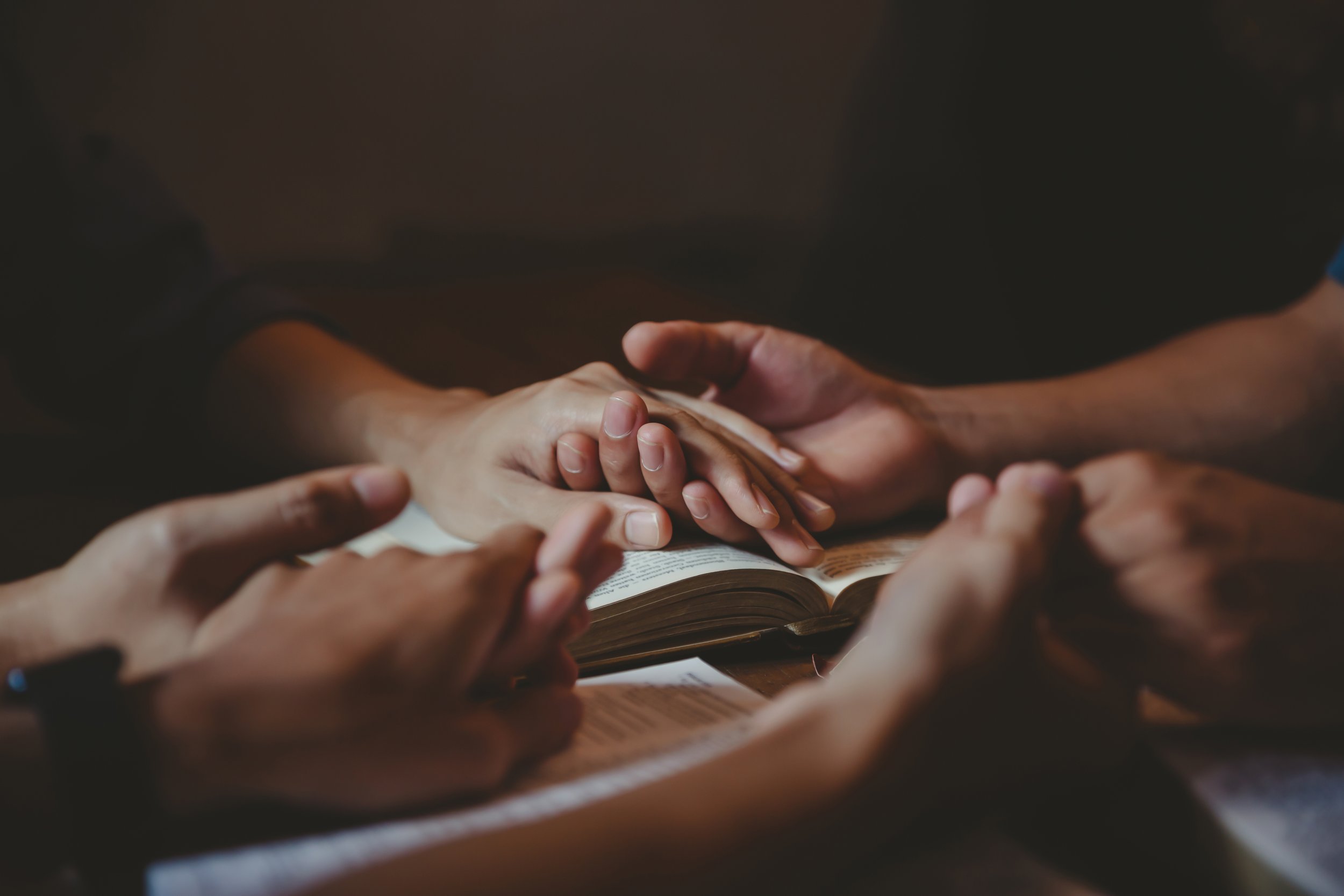 Multiple people praying together with hands touching a Bible for a Grace Capital City church worship service in Washington, DC.