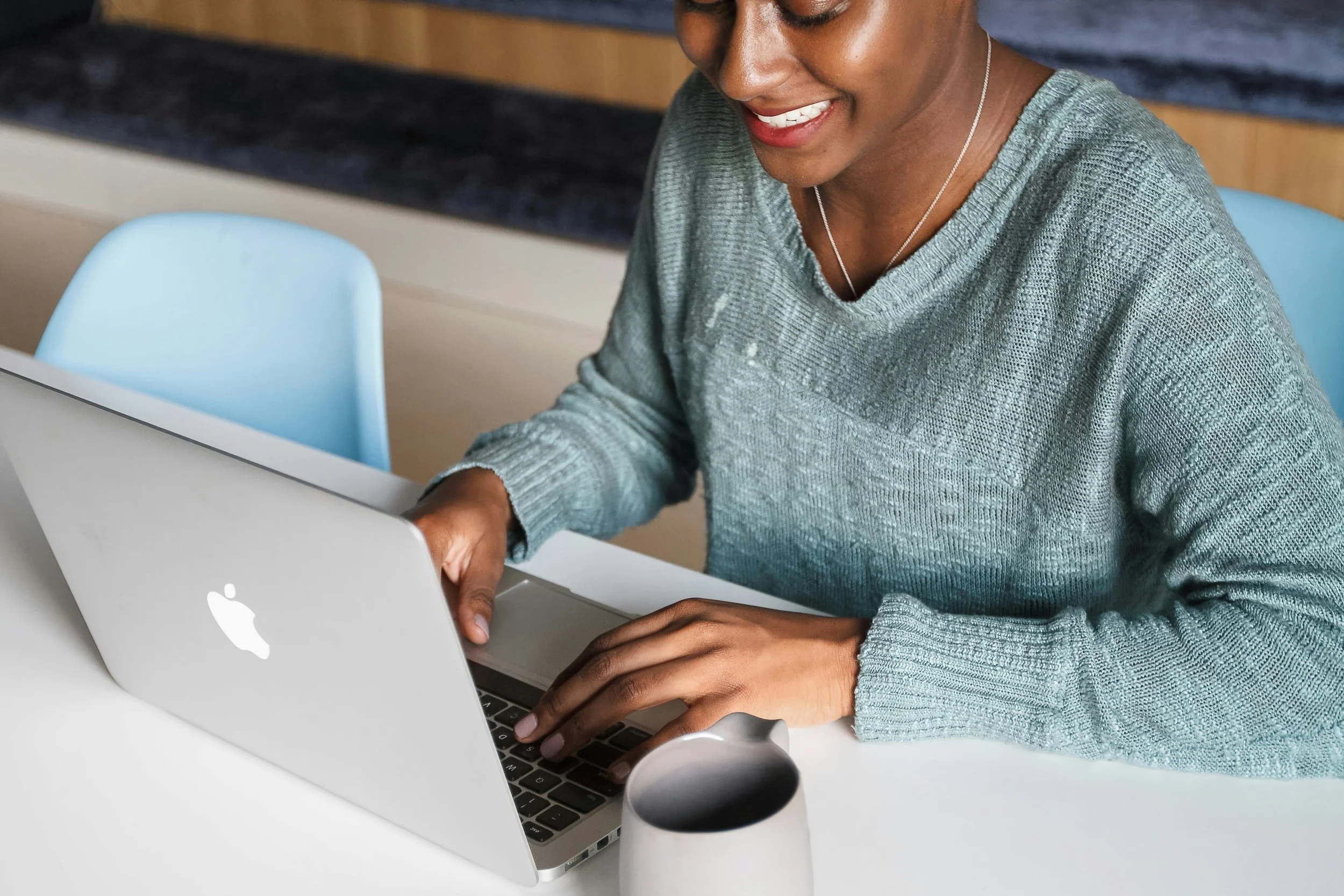 A woman using a silver MacBook laptop, smiling while working at a desk with a white mug nearby. This shows the connection resources at Grace Capital City, a church in Washington, DC.