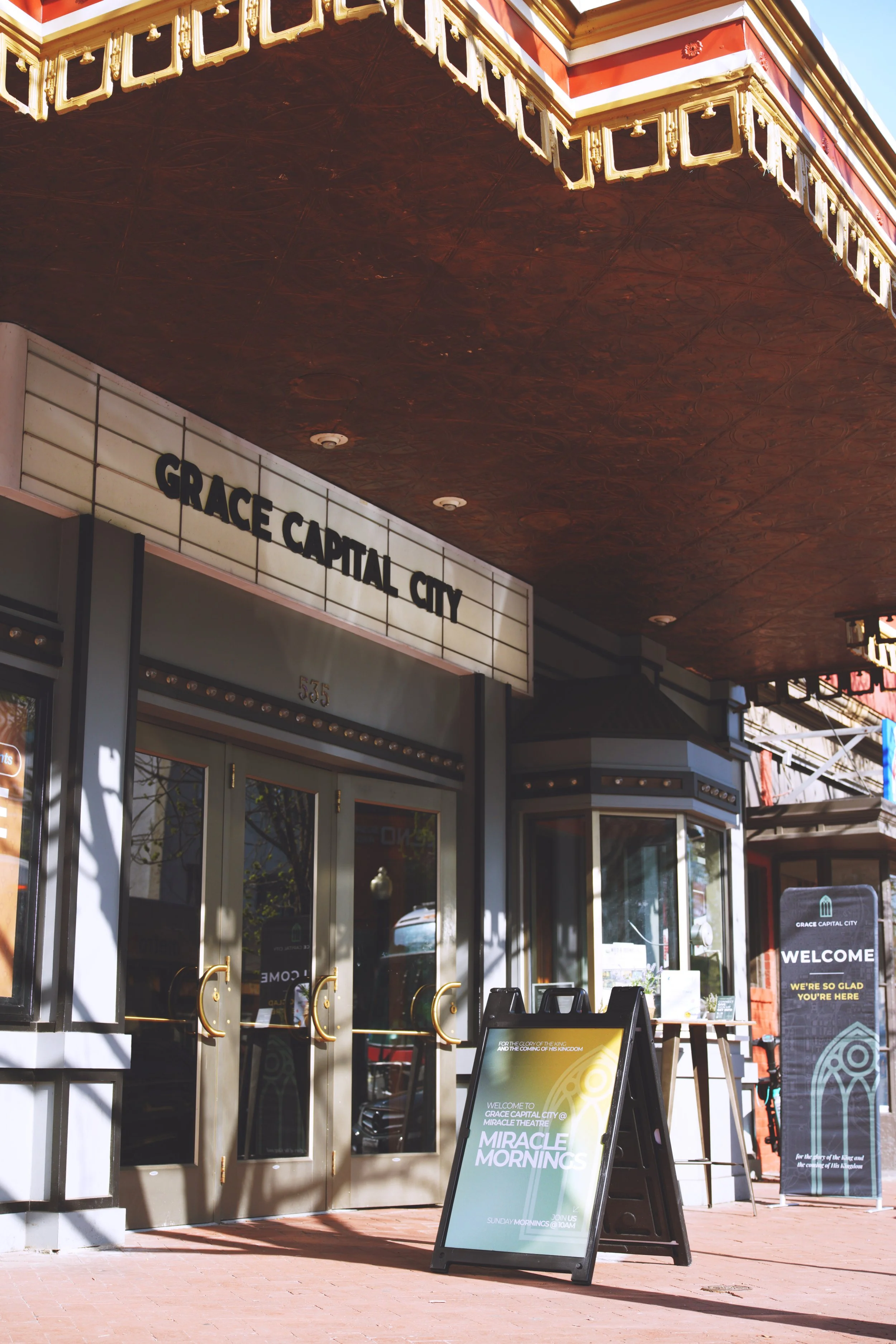 The entrance of Grace Capital City, a church that meets at Miracle Theatre in Washington, DC, , with a marquee sign that says, "Grace Capital City" and an A-frame signboard on a sidewalk outside, under a decorated awning.