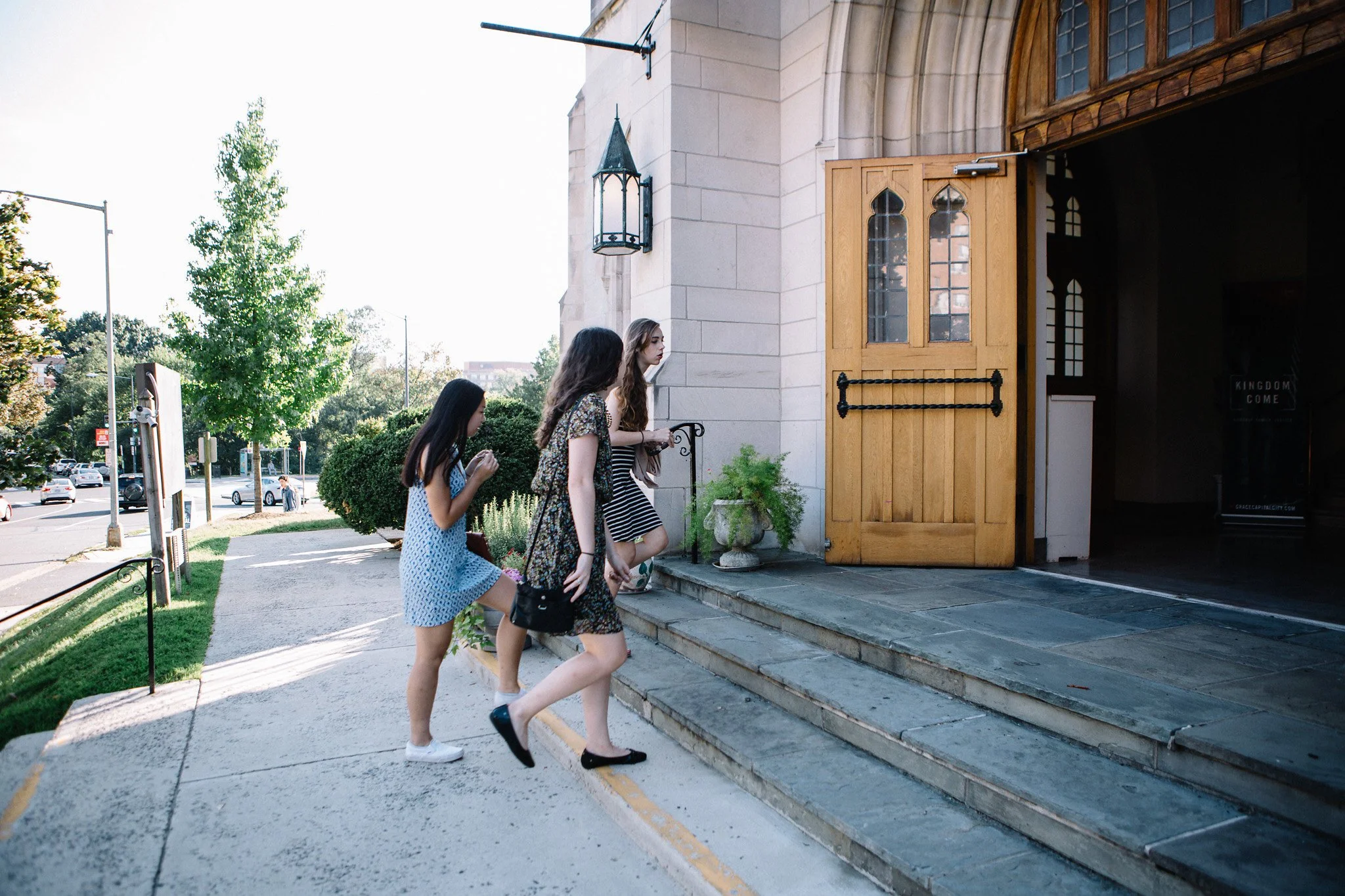 Three young women entering a church, climbing the steps at the entrance on a sunny day.