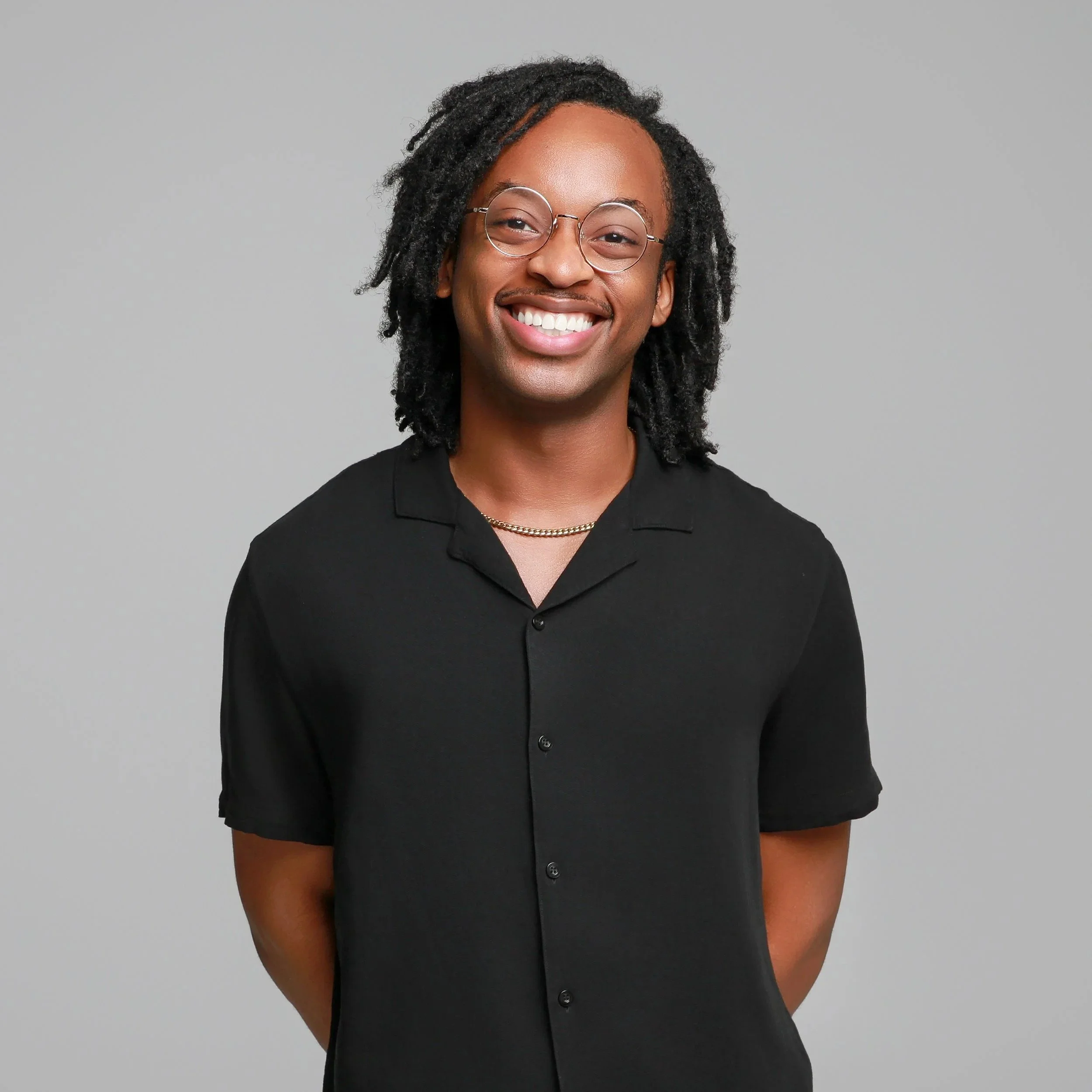 A smiling black man with glasses, wearing a black shirt, standing against a plain gray background. He is on staff at Grace Capital City, a church in Washington, DC.