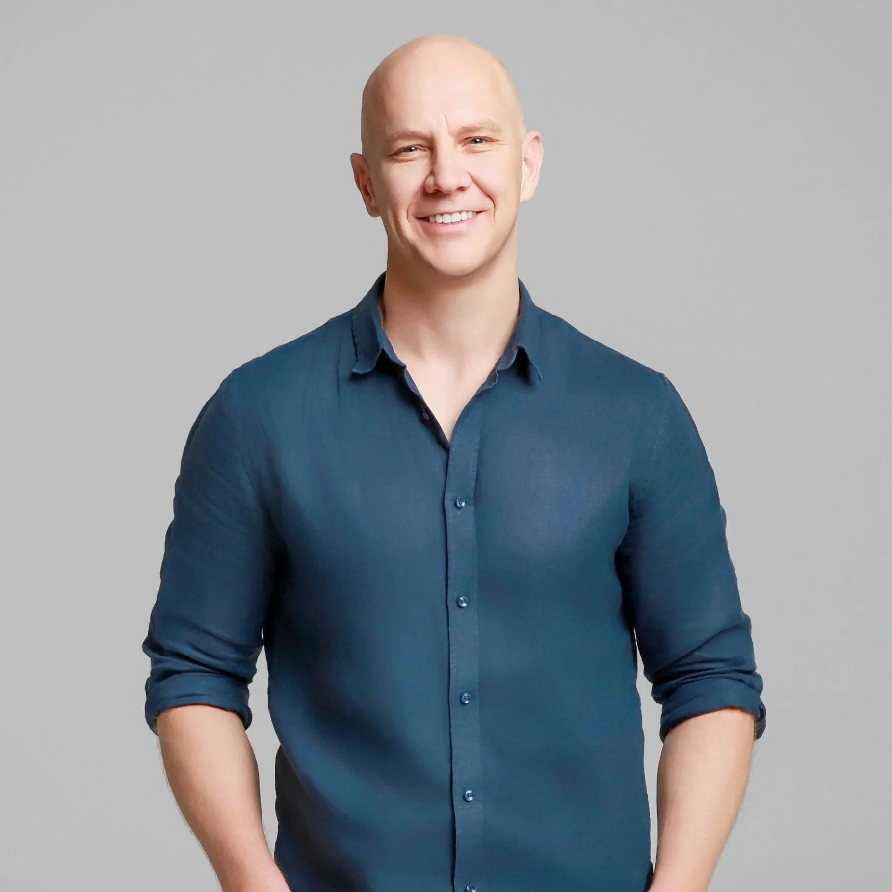 A smiling white man with no hair on his head and wearing a dark blue shirt against a gray background. He serves as the Lead Pastor at Grace Capital City, a church in Washington, DC.