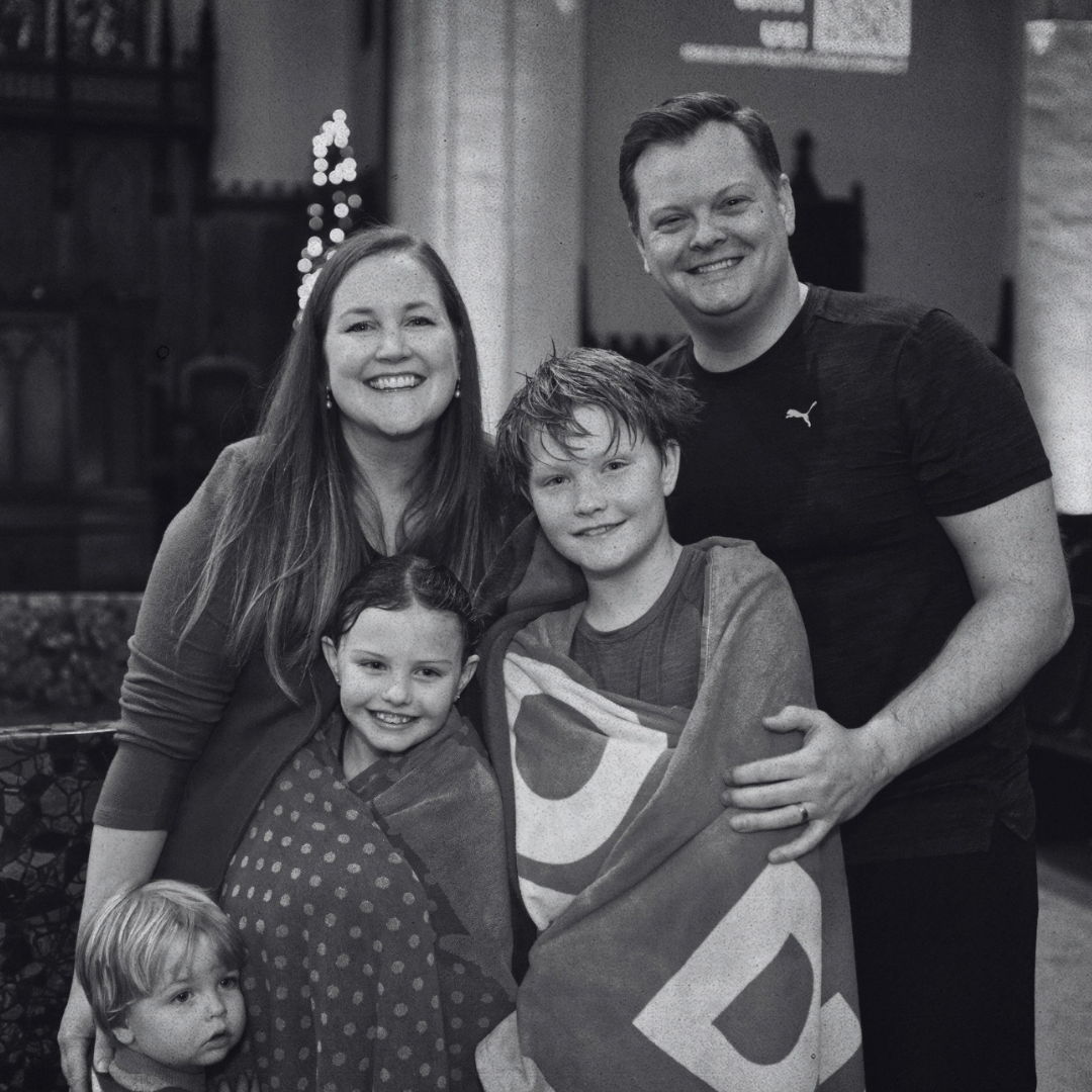 A black and white photo of a smiling, happy family of five, with two adults and three children, after a baptism during a Grace Capital City church worship service in Washington, DC.