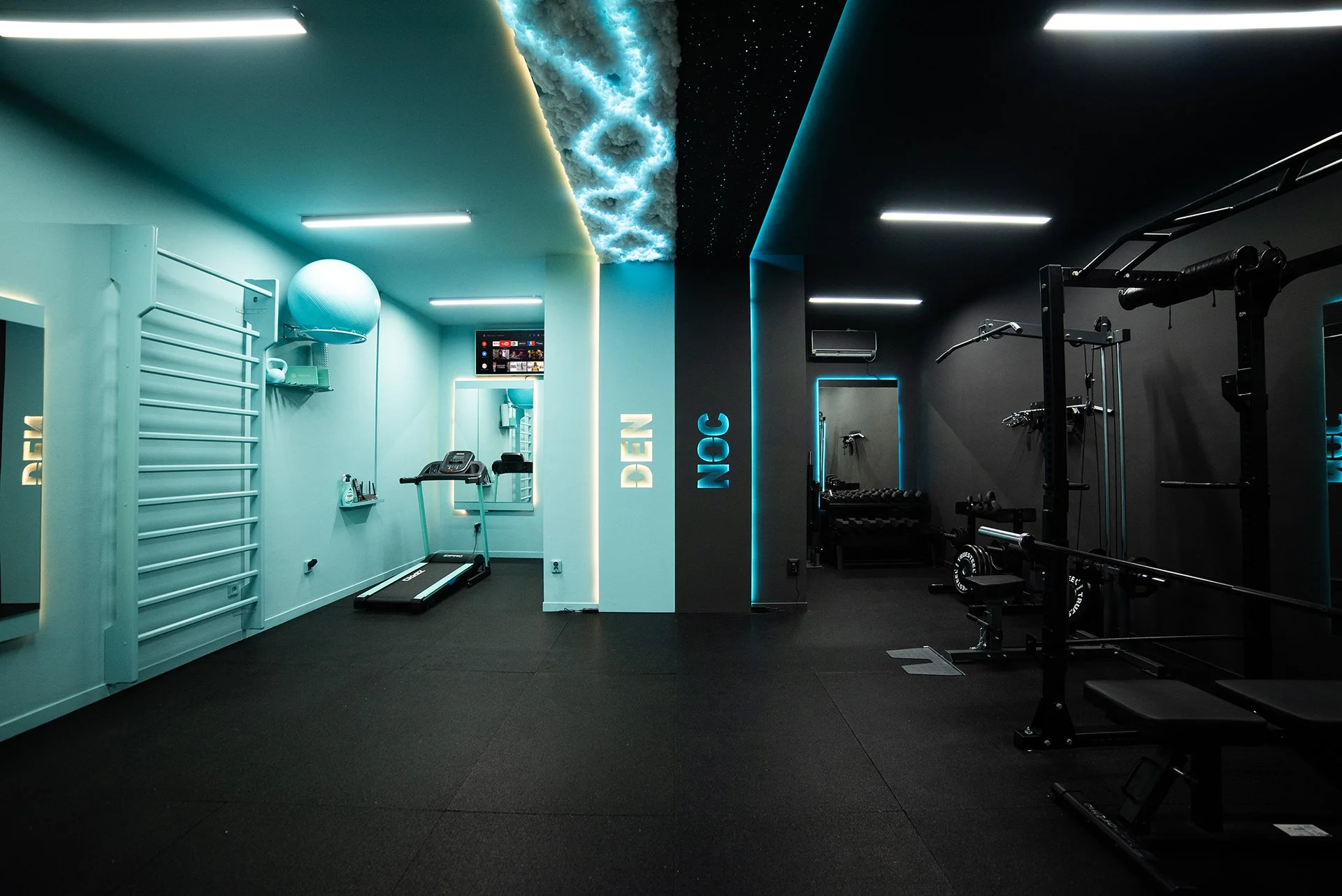 This is a modern gym with a split color theme, featuring a turquoise side labeled 'DEEN' and a dark side labeled 'NCC'. The turquoise area has a treadmill, a medicine ball, and a wall-mounted ladder, while the dark side has weightlifting equipment, a mirror, and a small seating area. The ceiling has unique cloud-like structures and starry lights.
