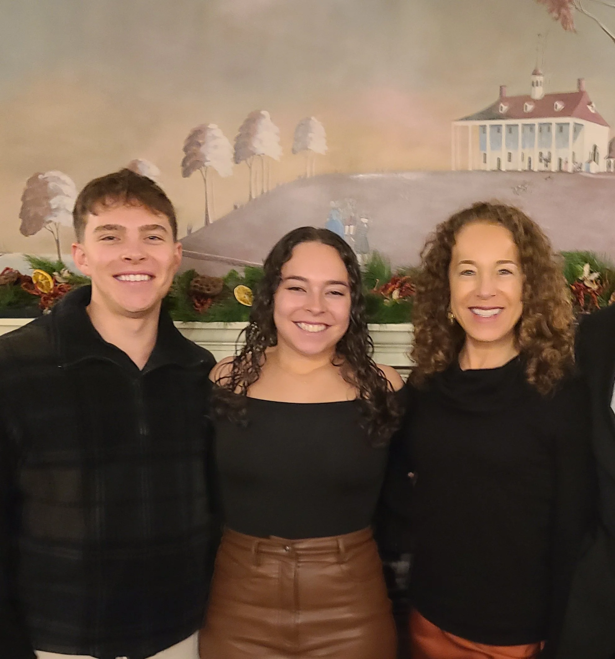 A mom with her adult son and daughter, smiling, standing in front of mural.