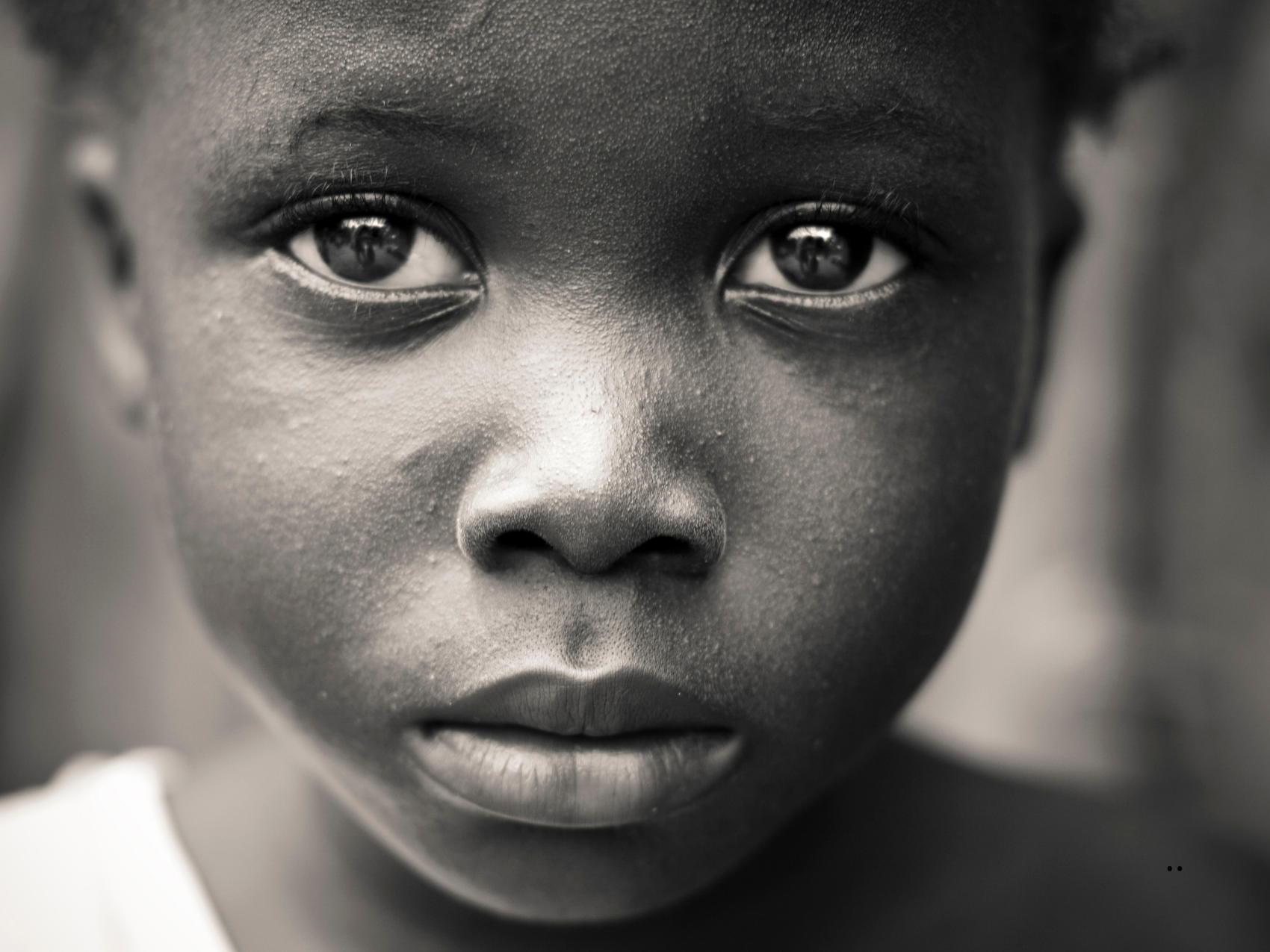 Primer plano en blanco y negro del rostro de una niña de piel oscura, mirando directamente a la cámara con expresión seria.