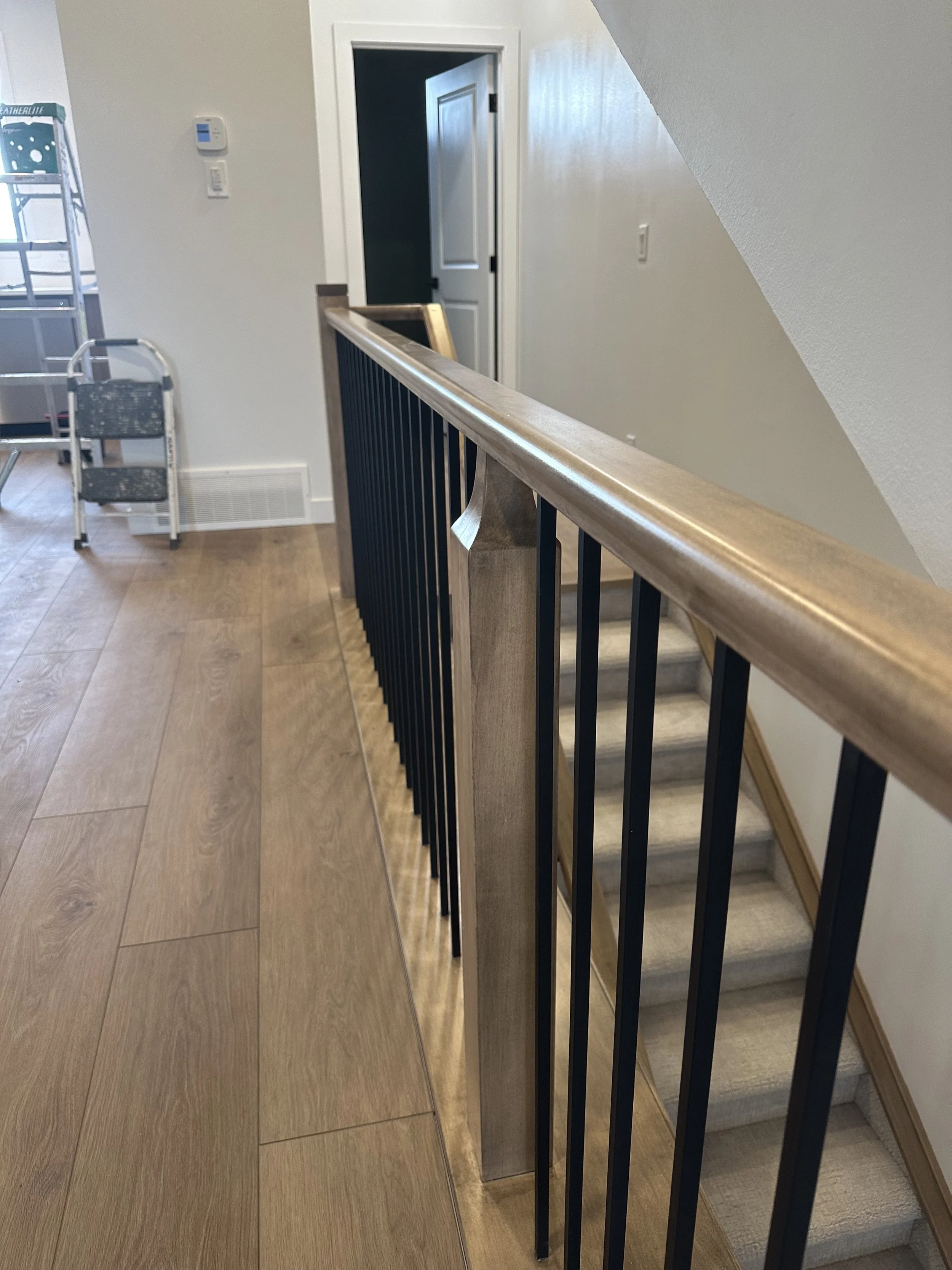 View of a staircase with a wooden handrail and black metal balusters in a home interior.