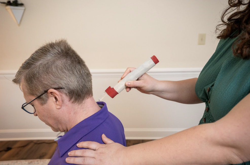 A woman administering a chiropractic adjustment to a man with glasses, who is leaning forward.