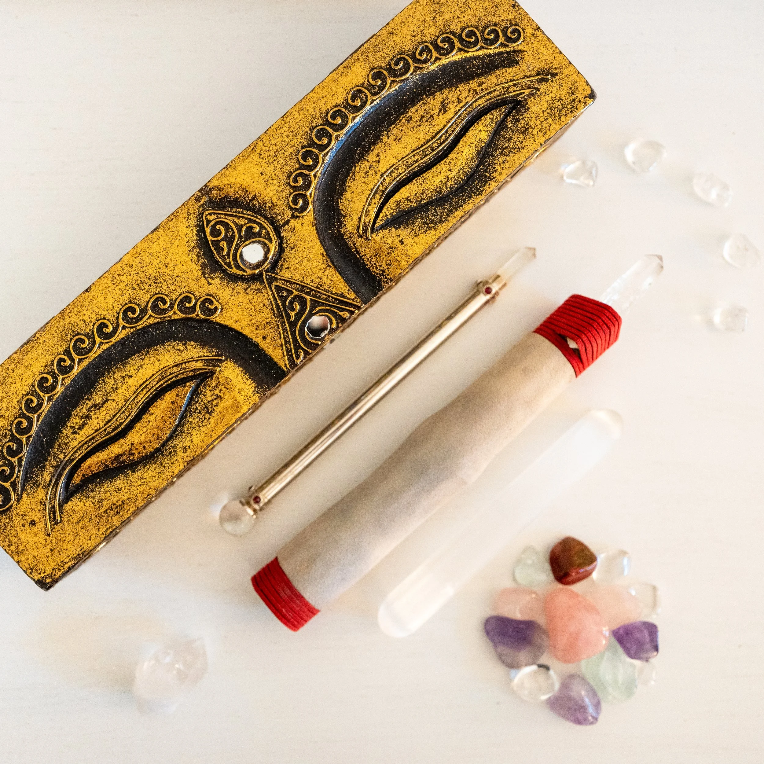 A tarot card, a glass prism, a scroll, and various crystals and gemstones on a white surface.