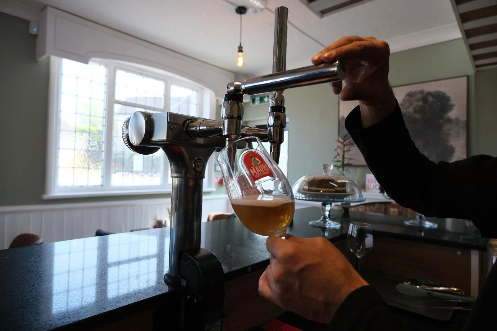 Person filling a glass with beer from a tap in a cafe or bar.
