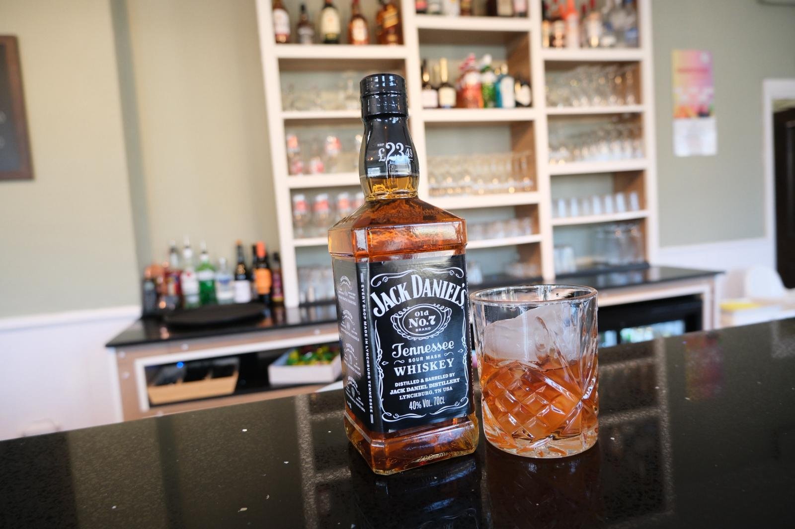 A bottle of Jack Daniel's Tennessee Whiskey and a glass with ice and whiskey on a bar counter.