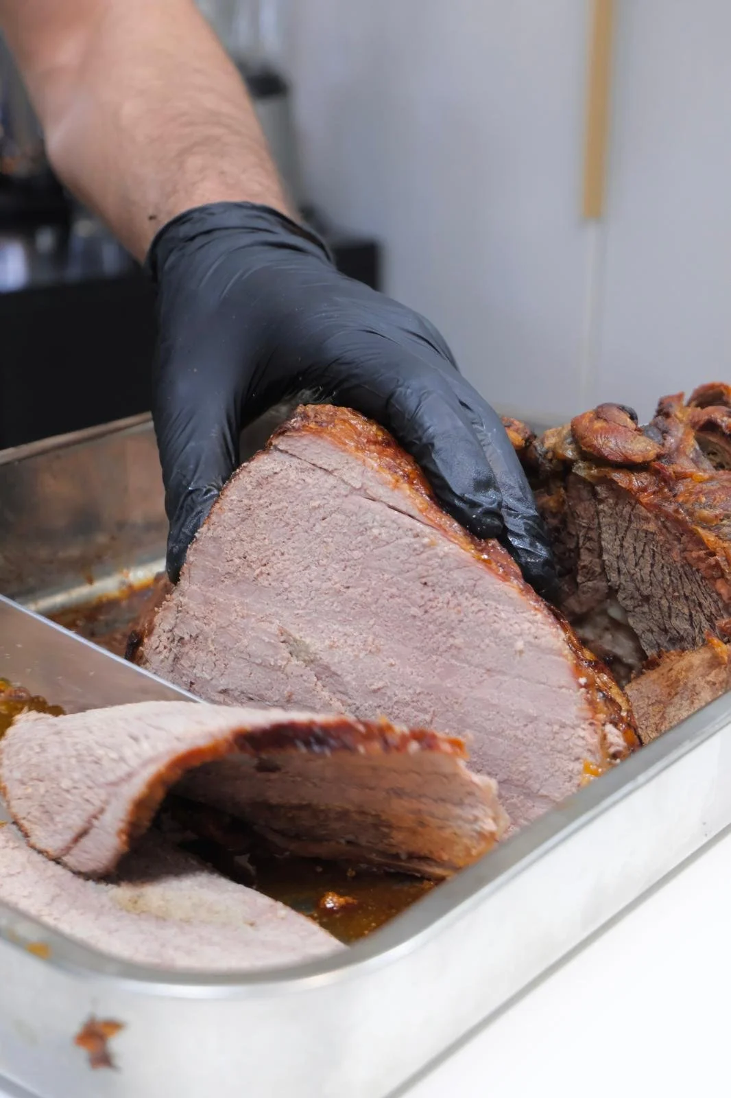 A person wearing black gloves slicing a large cooked beef roast in a metal tray.