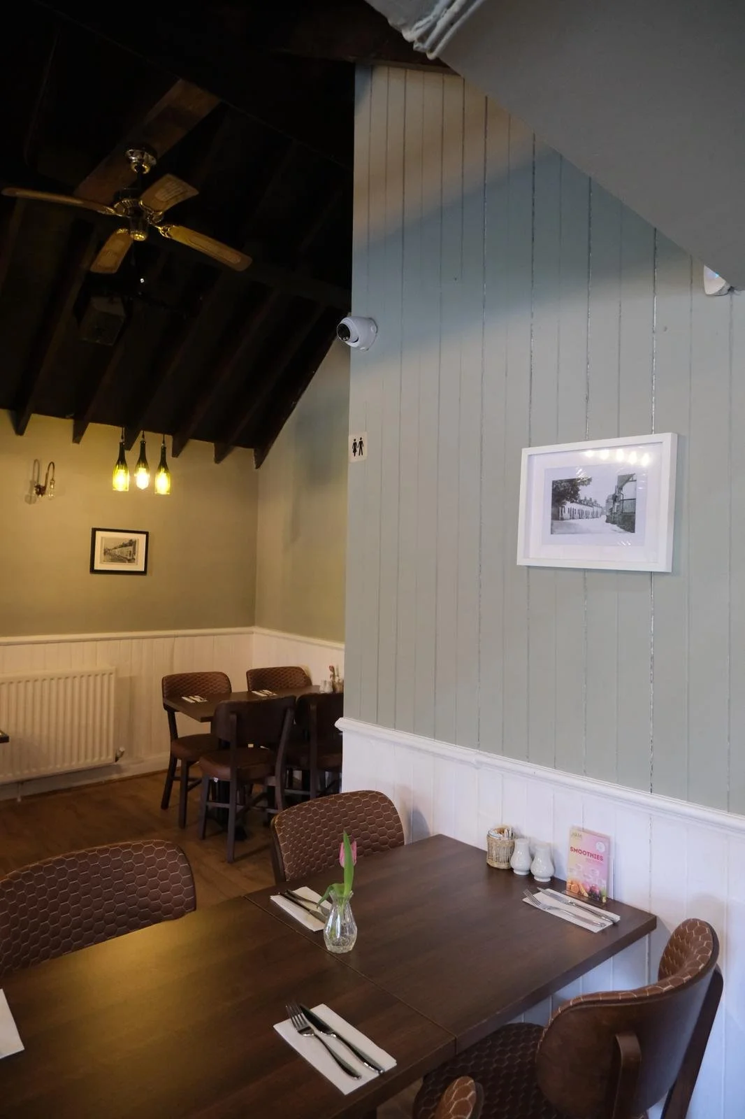 Interior of a cozy restaurant with wooden tables, patterned chairs, framed pictures on the walls, and soft lighting.