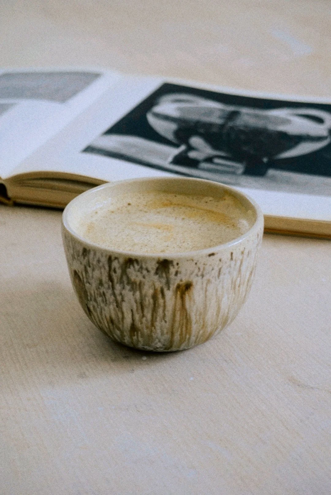 Ceramic cup with coffee or chamomile tea in front of an open book that has black and white images.