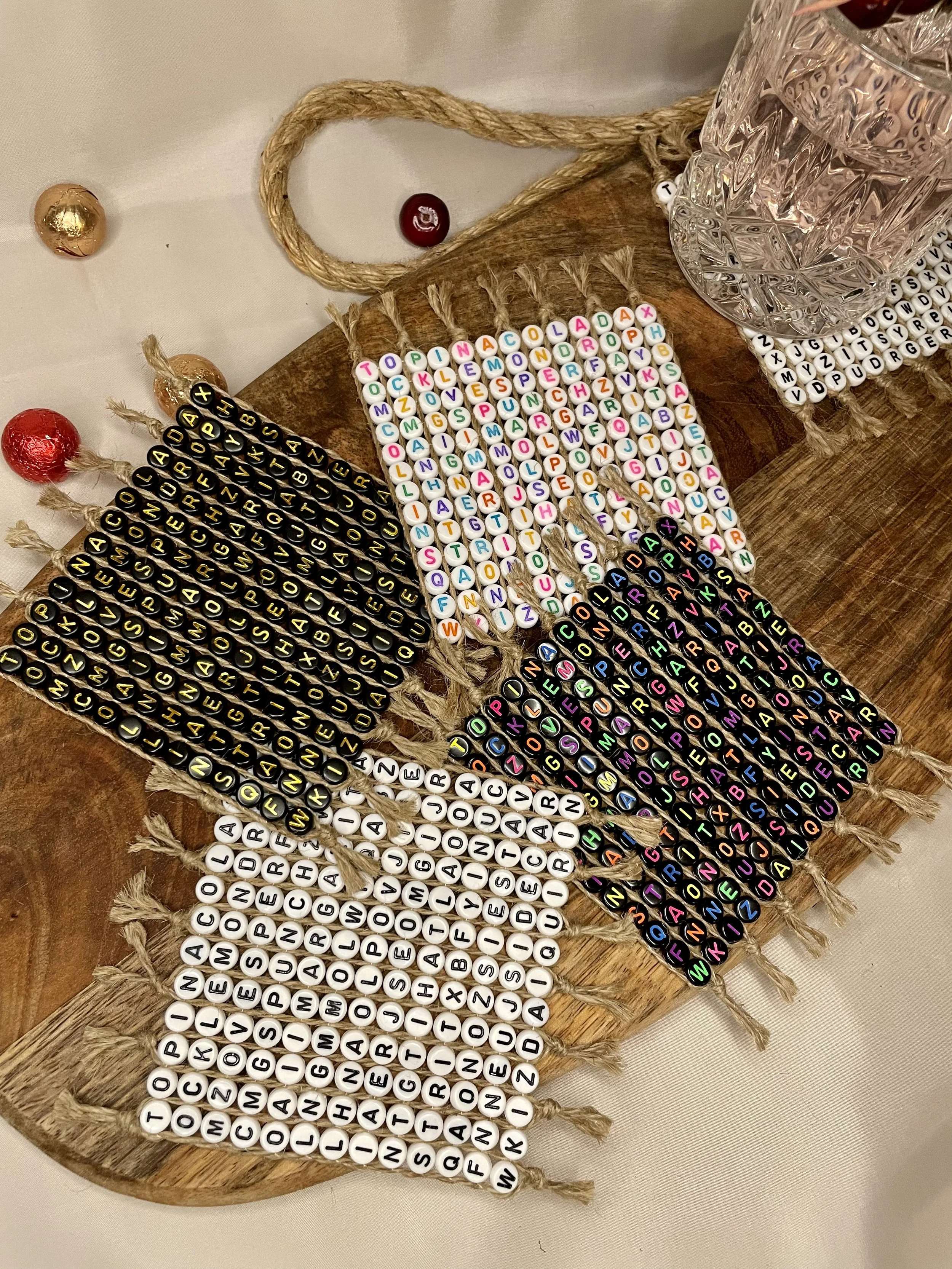 Colorful beaded coasters with alphabet beads, displayed on a wooden board on a table.