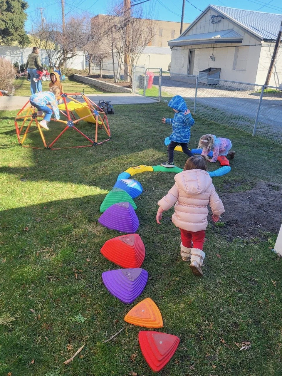 Children playing in a backyard with playground equipment and colorful stepping stones.