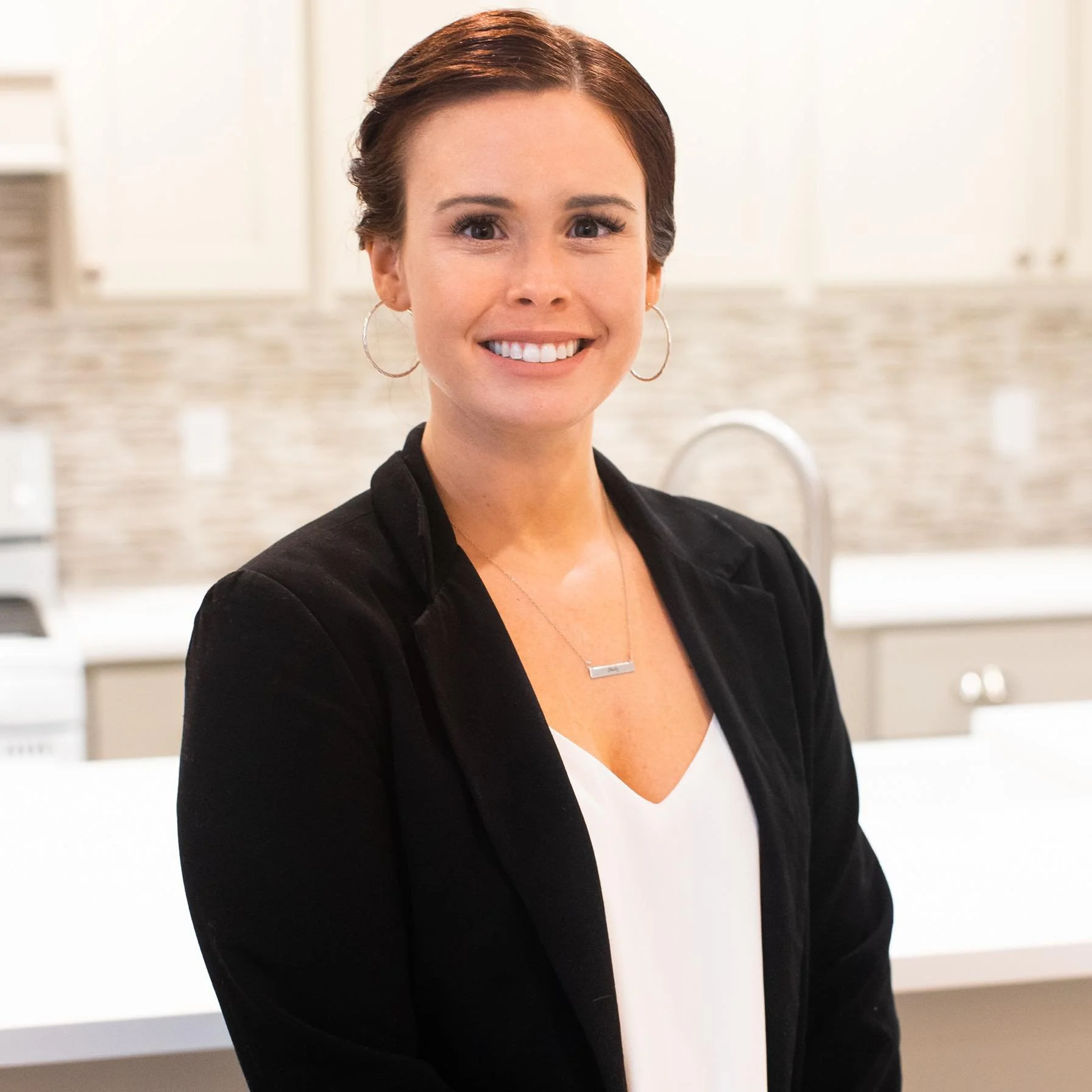 Madaline Stultz. President of Pend Oreille Family Cooperative. A smiling woman with short brown hair, hoop earrings, wearing a black blazer over a white top, standing in a modern kitchen.
