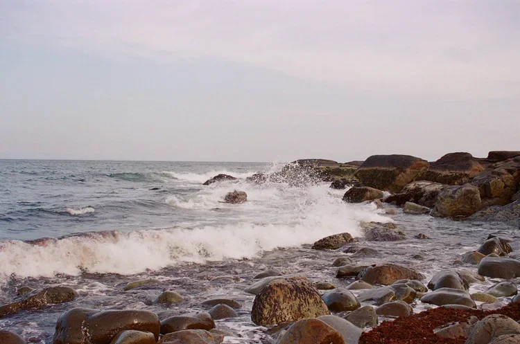 Rocky shoreline with waves crashing against the rocks under a cloudy sky.