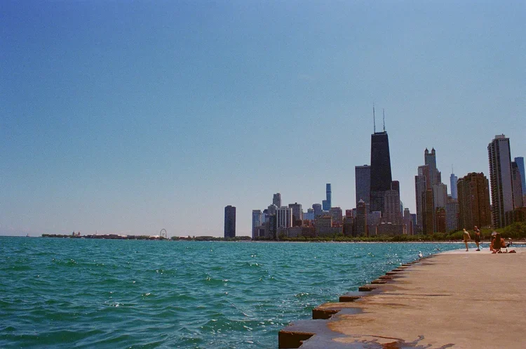 Skyline of Chicago with tall buildings and the lakefront, people walking on the pier along Lake Michigan.