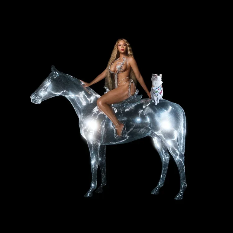 A woman with long blonde hair posing nude with a star-shaped pasty, sitting on a shiny, illuminated horse sculpture, with a small dog wearing a colorful sweater on the horse's back, against a black background.