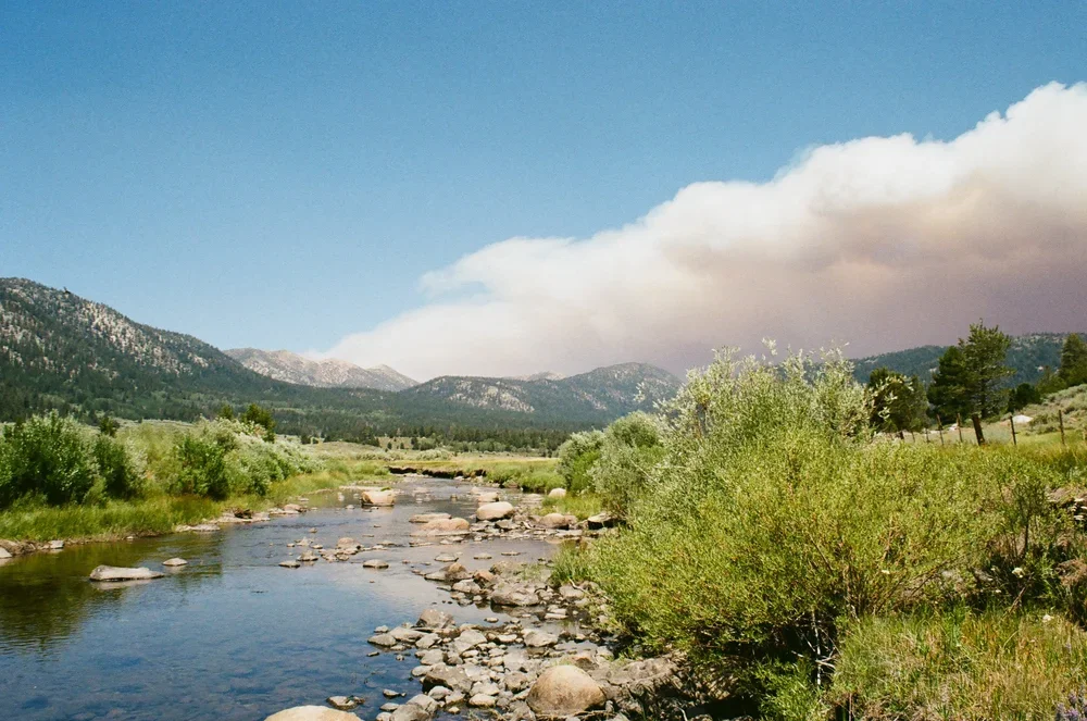 A peaceful river flowing through a lush green valley with mountains in the background and a partly cloudy sky.