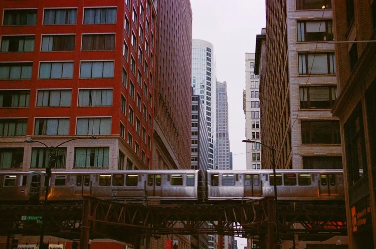 A train traveling on an elevated track through a dense urban cityscape with tall buildings surrounding it.