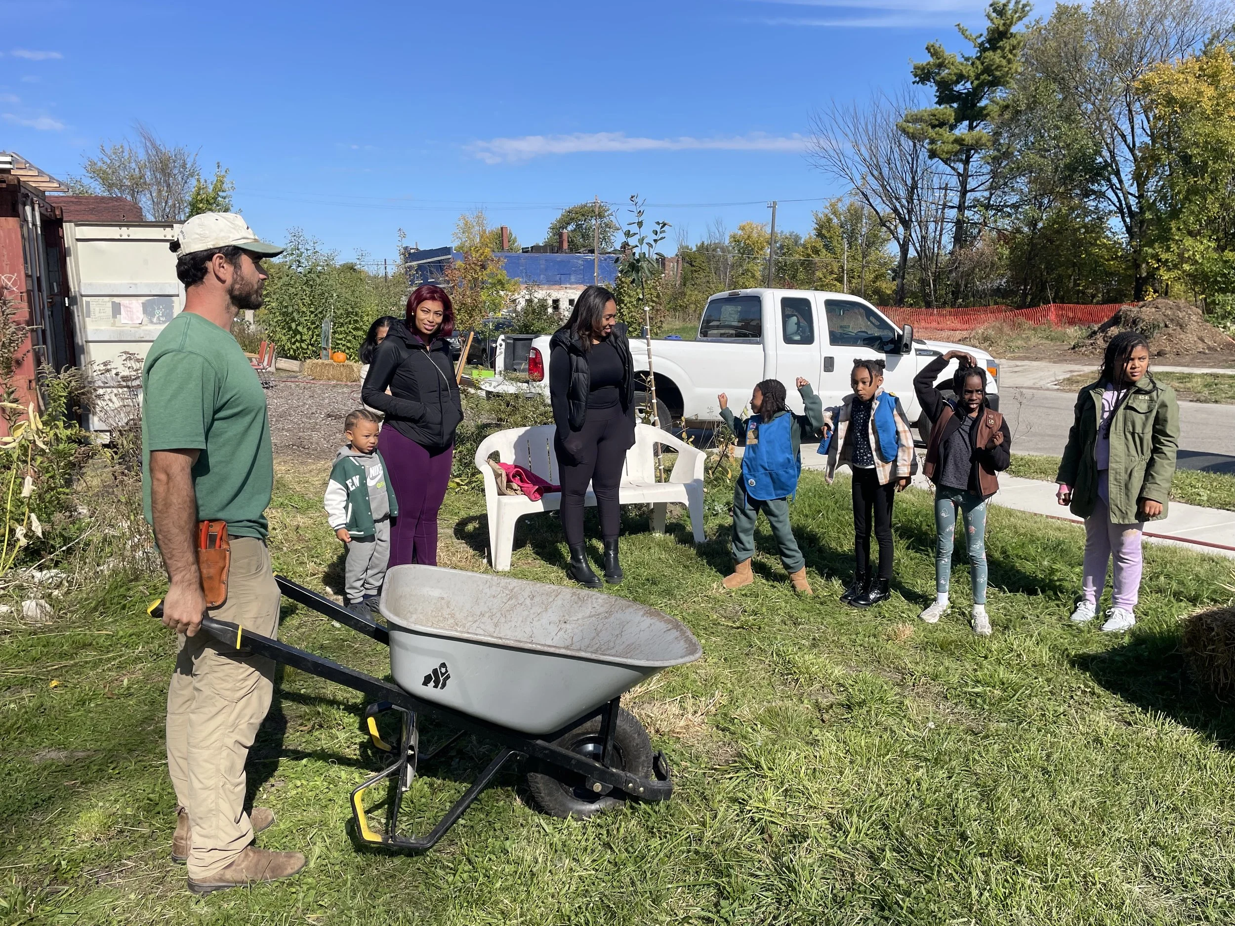 A person holding a wheelbarrow in front of a small group of people