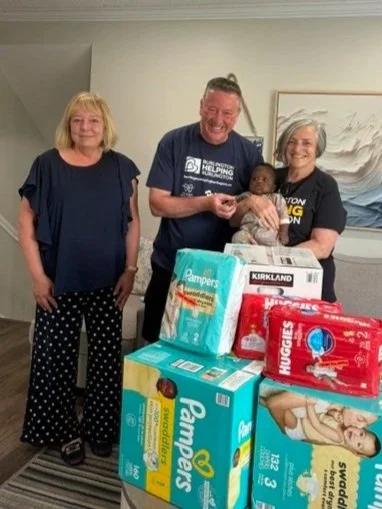 Sean Campbell and Vicki Trottier donate Bats for Diapers Drive diapers off at Shifra Homes. Vicki and Sean are holding a baby wearing a gray sleeper with leader of Shifra Homes posing at far left.