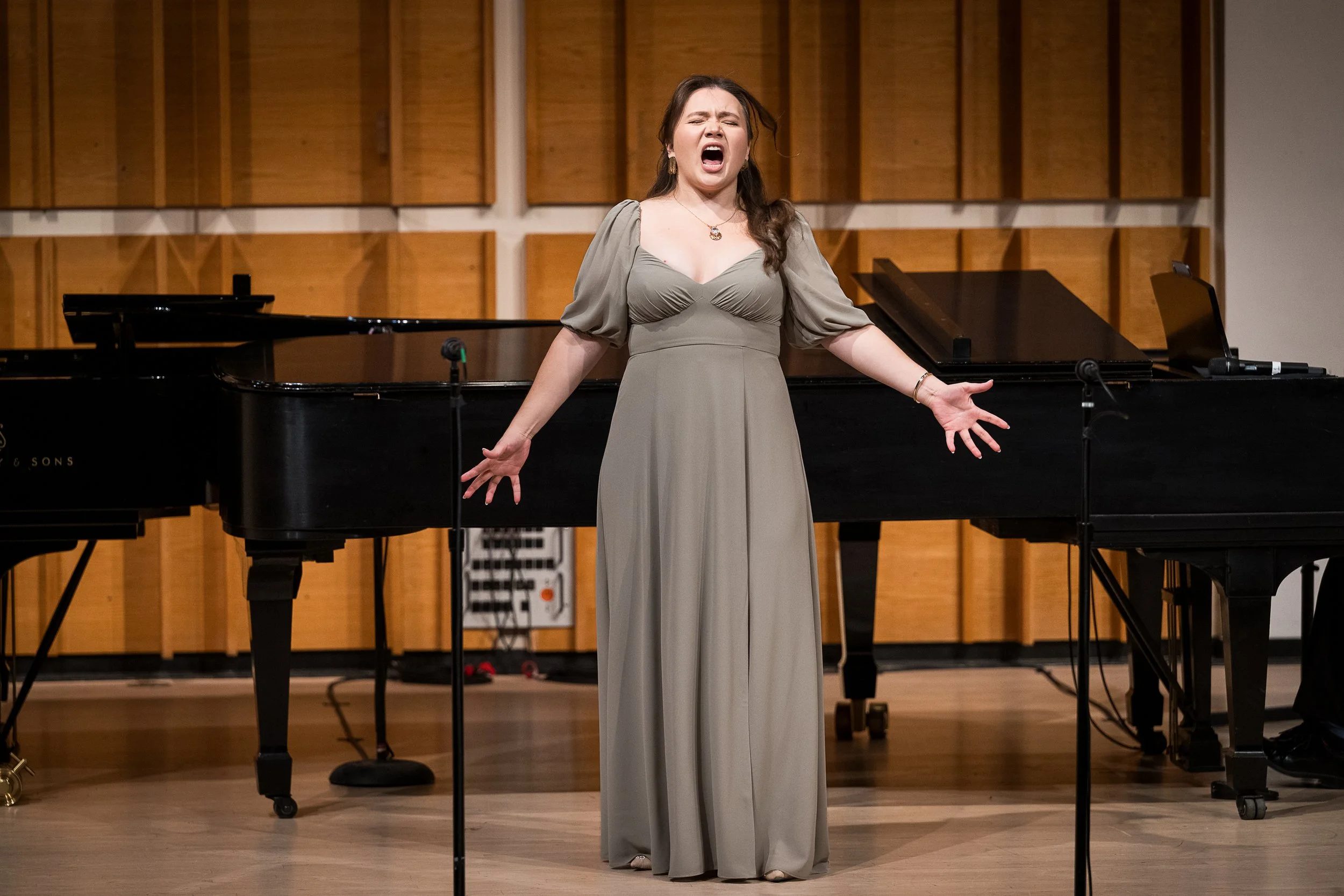 A woman singing passionately on stage with a grand piano and sound equipment in the background.