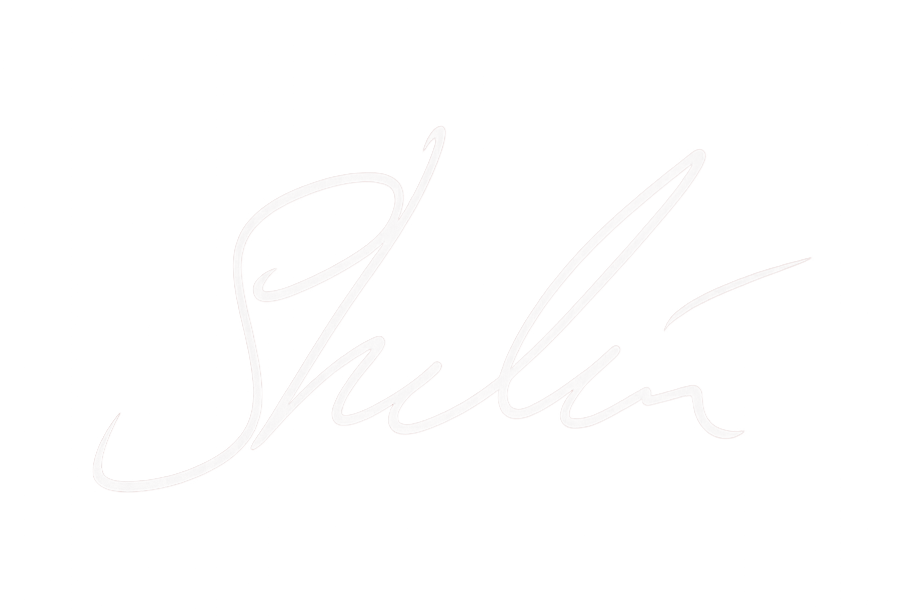 The image features a white handwritten signature on a black background that reads 'Shalia'.