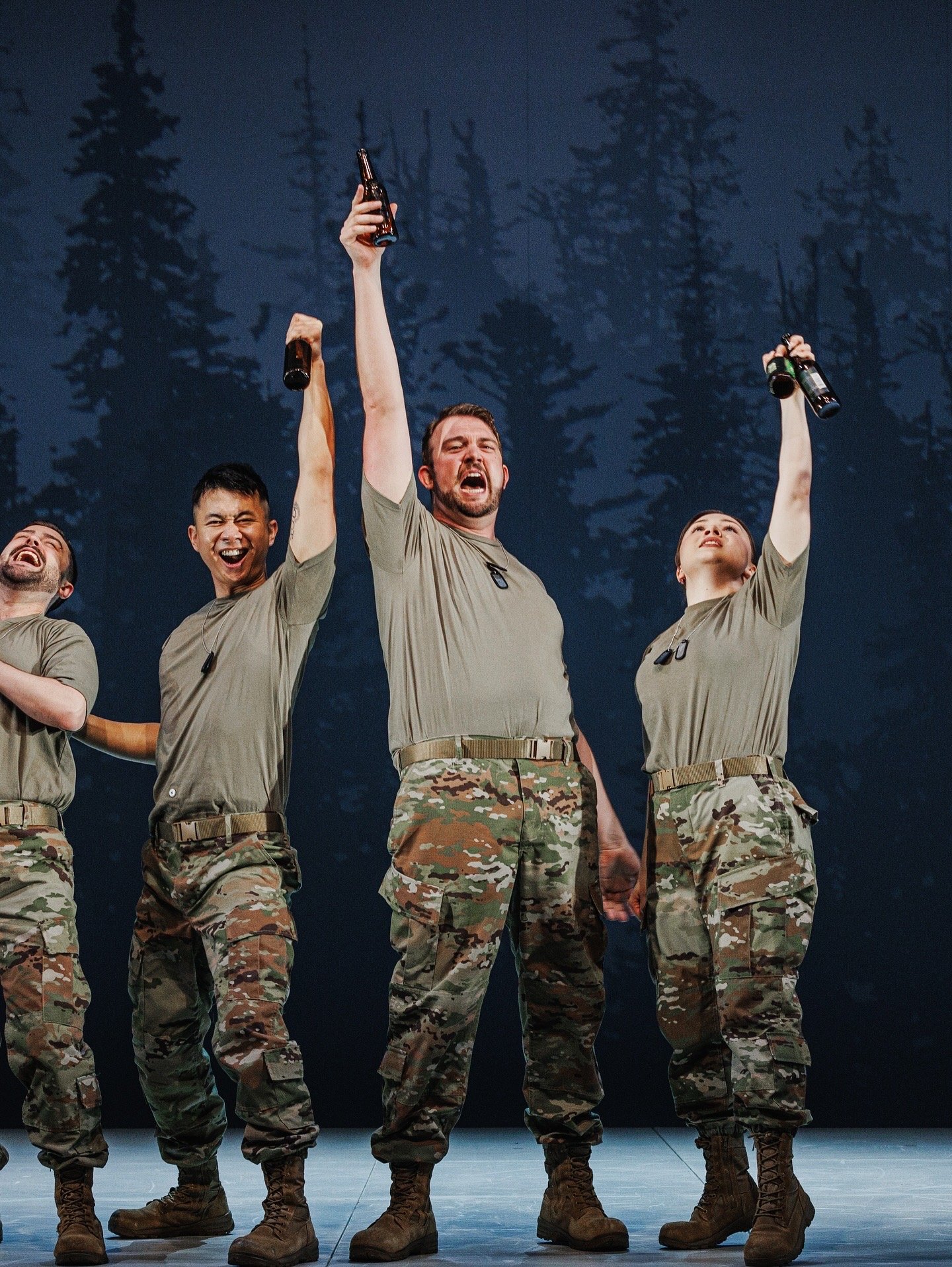 A group of soldiers in uniform standing on stage, cheering and raising bottles of beer in the air.