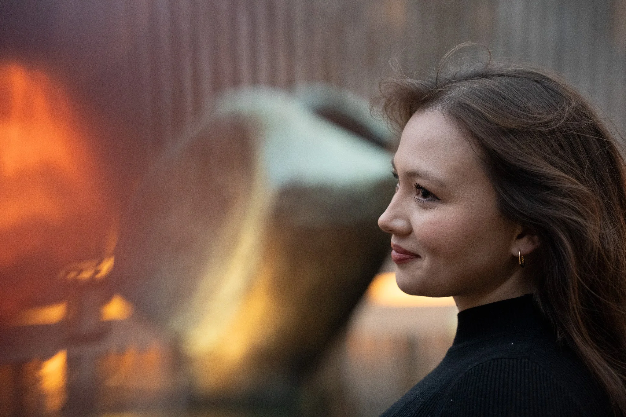 A woman with wavy brown hair and hoop earrings looking at a fire.