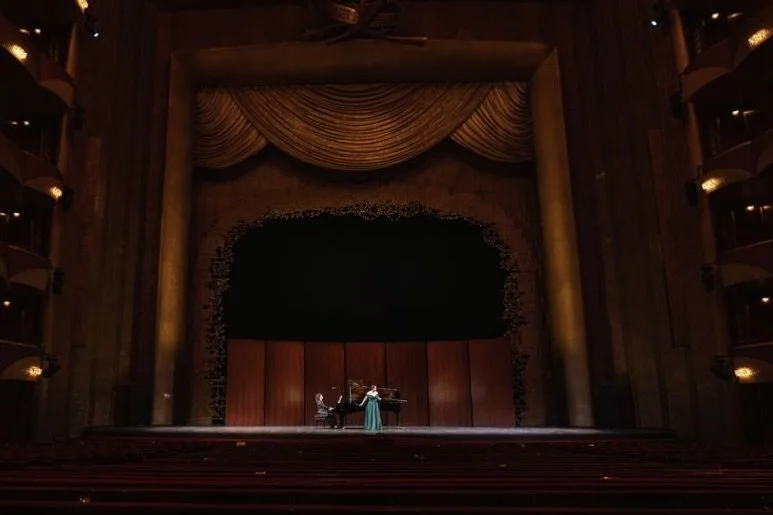 A woman in a long dress playing the piano on a stage in a theater
