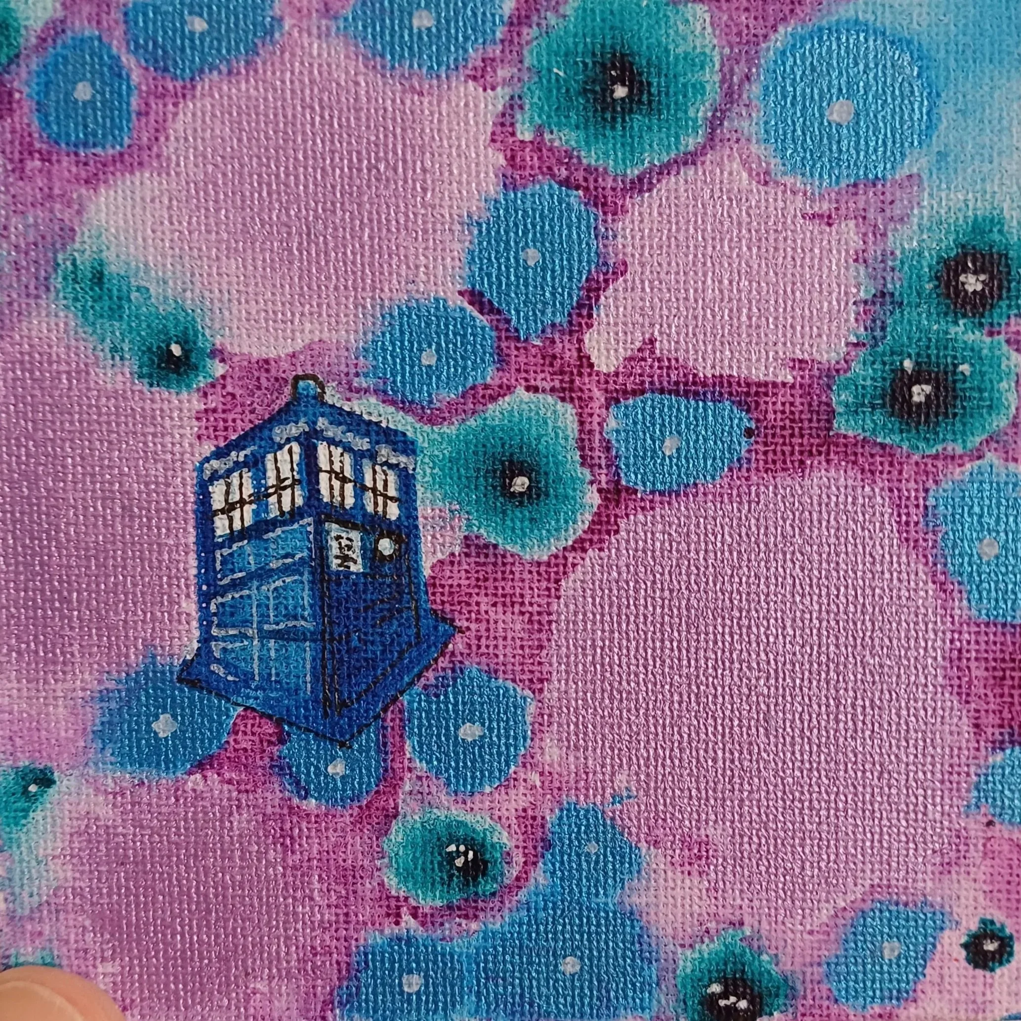 Close-up of fabric with a pattern of blue and teal flowers on a pink background, featuring a small blue illustration of the TARDIS from Doctor Who.