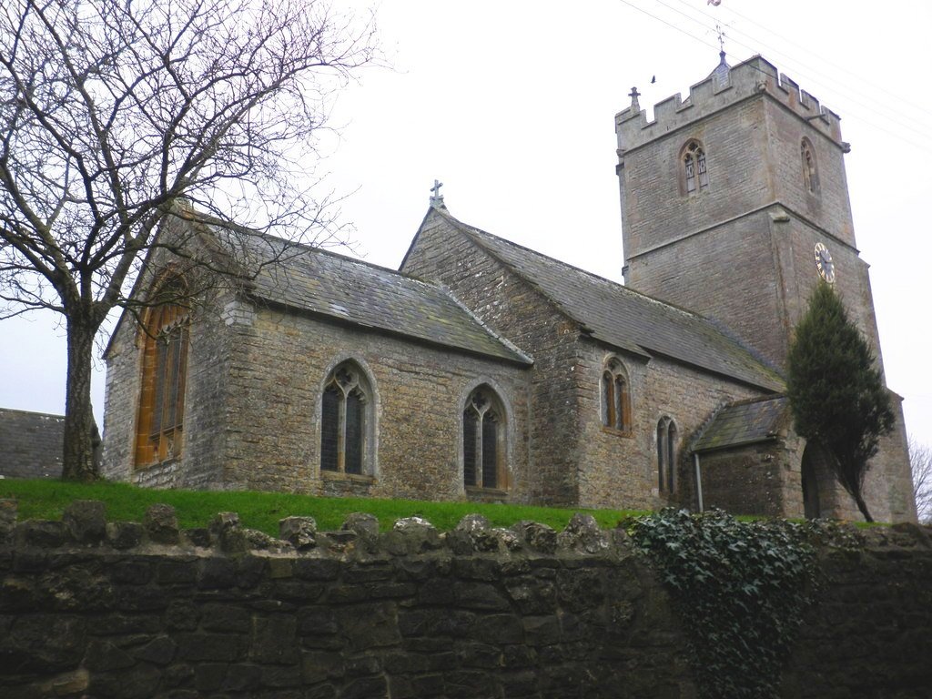 St Michael & All Angels Church with a tall clock tower, arched windows, surrounded by trees and a stone wall.