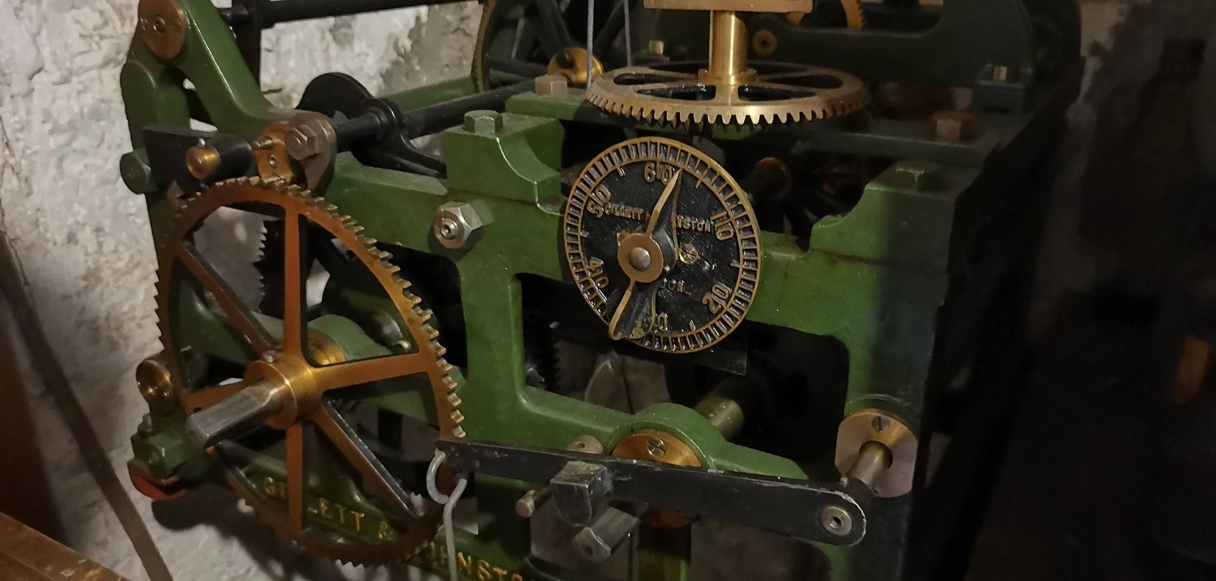 Close-up of a vintage mechanical clockwork with green and brass components, including gears, wheels, and a black dial.