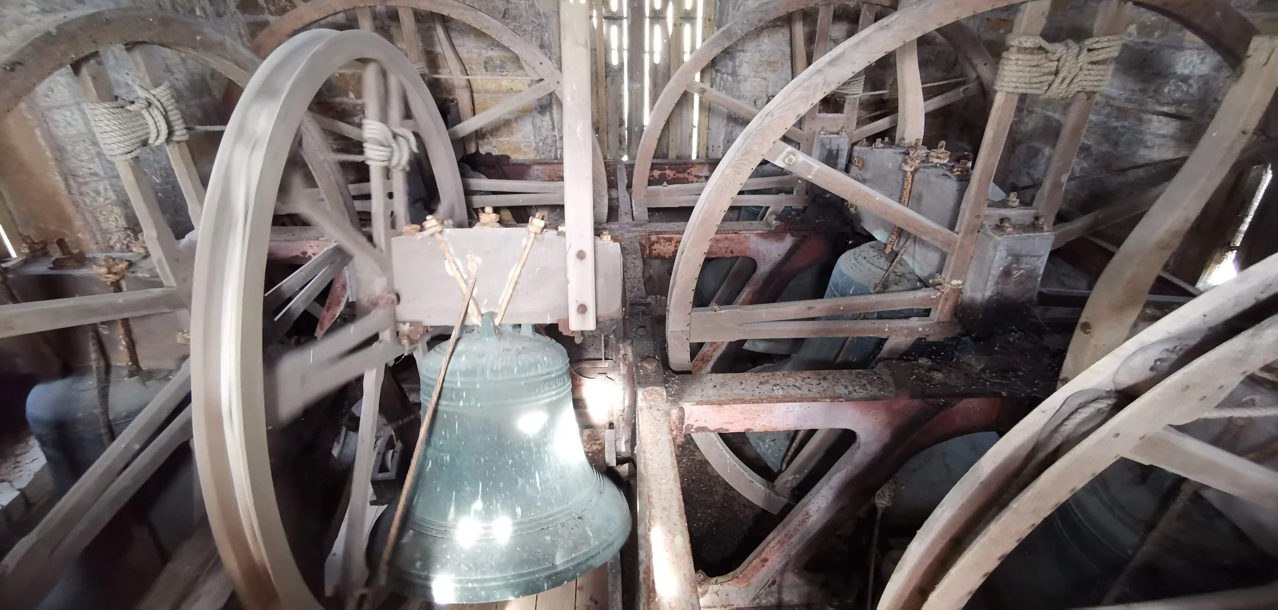 Close-up view of the inner mechanism of a large, old church bell with wooden wheels and metal components, possibly part of a bell tower's clock or ringing system.