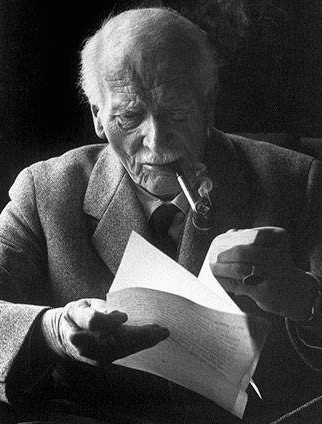 An elderly man with white hair and a beard, smoking a cigar, reading a document.