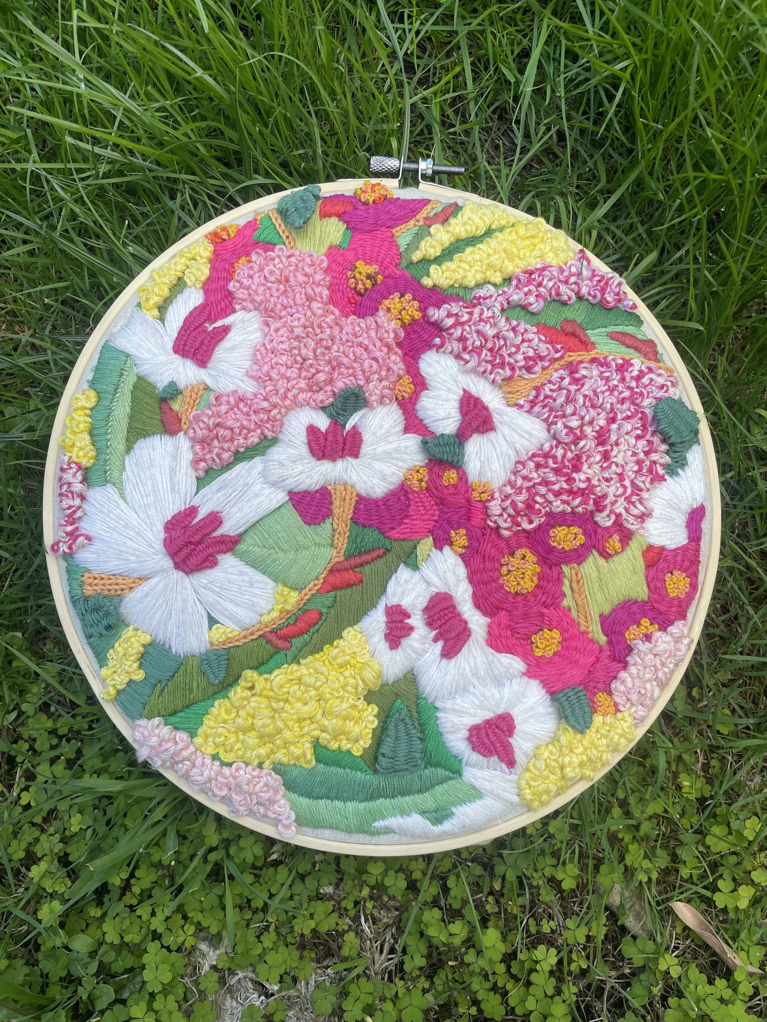 Colorful embroidered floral fabric in a circular embroidery hoop placed on green grass.