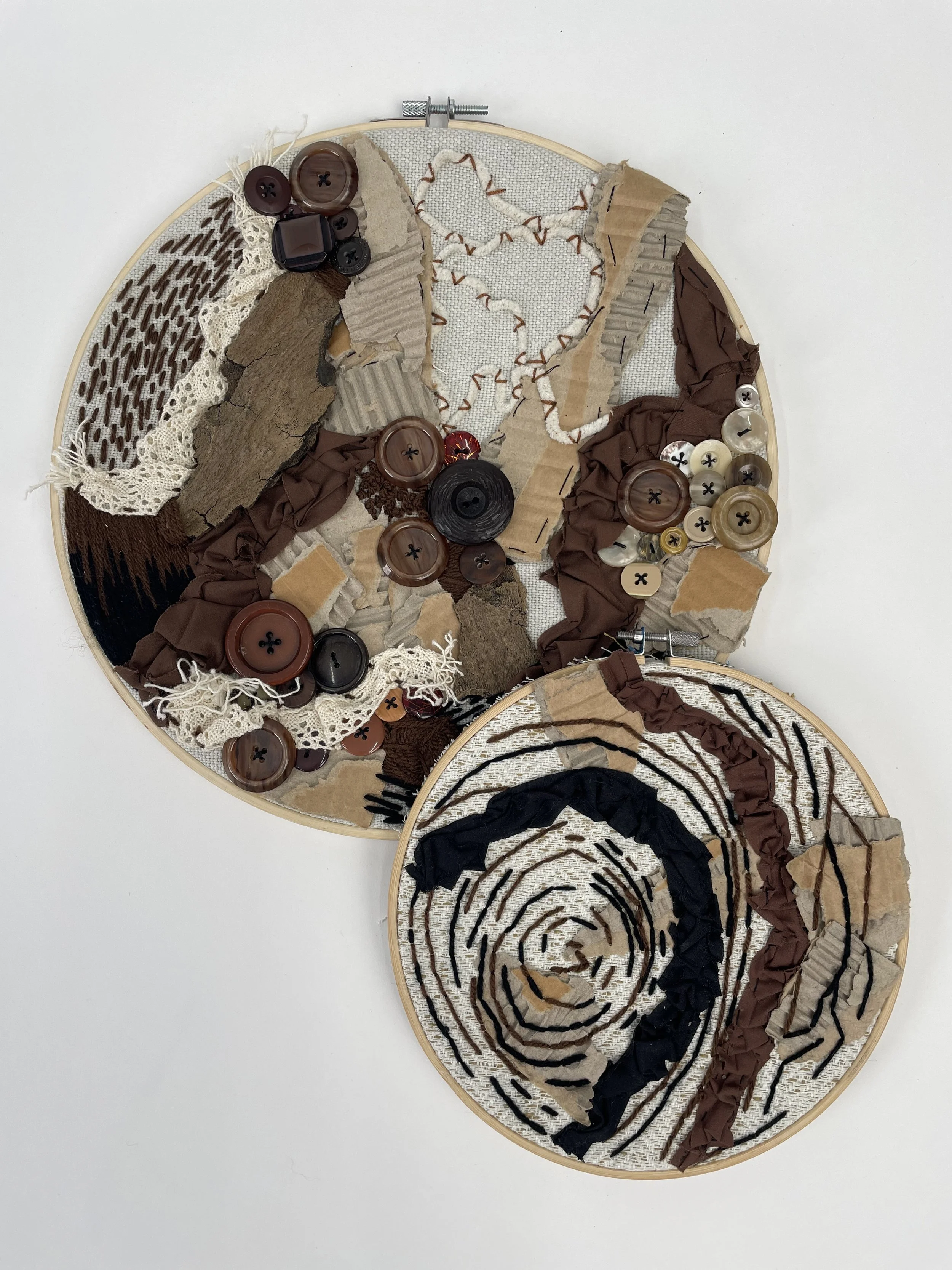 Two embroidery hoops with textile art, buttons, and fabric scraps in earthy tones, arranged on a white background.