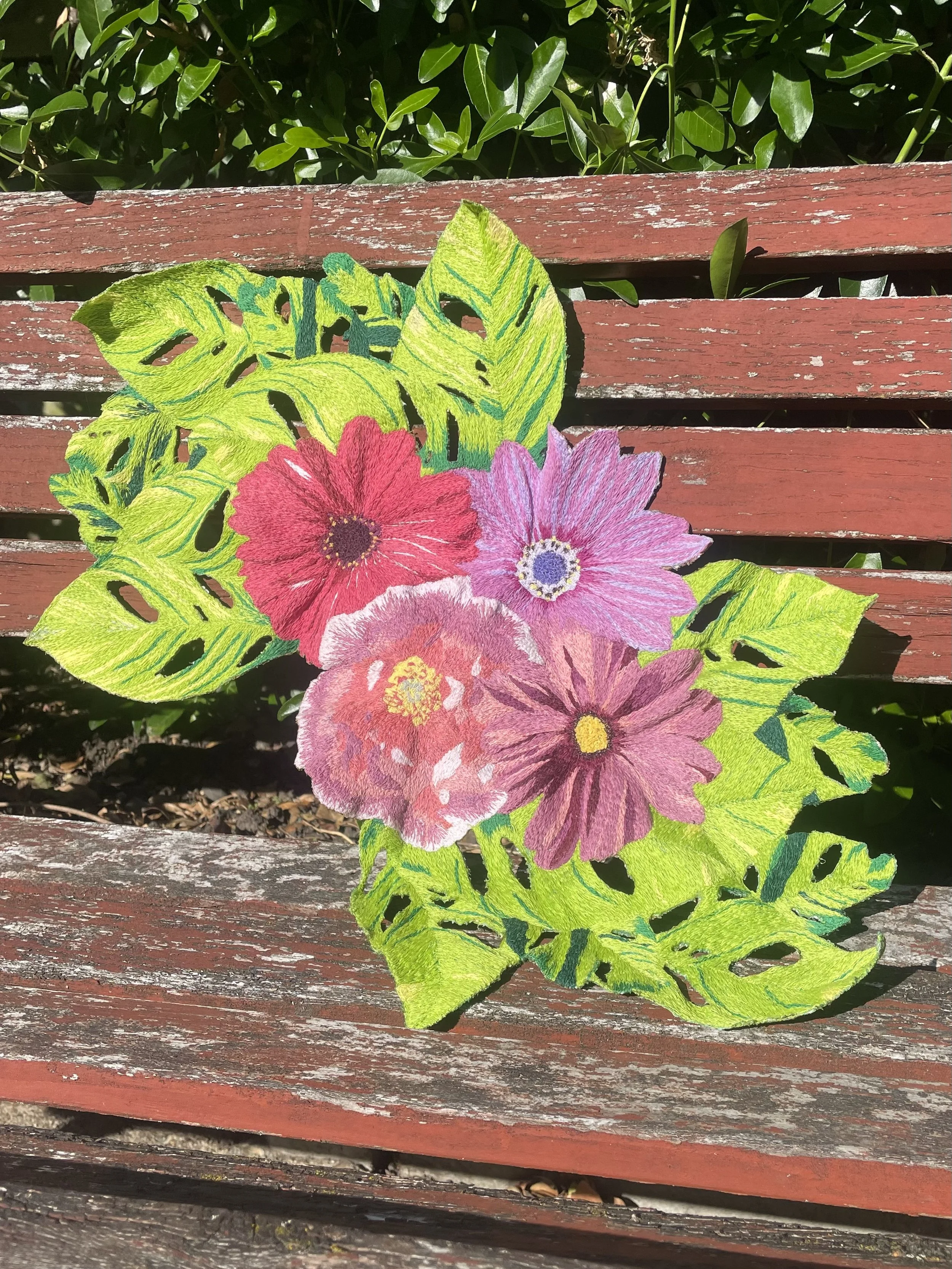 Colorful embroidered cloth with pink and purple flowers and green leaves, placed on a weathered red wooden bench outdoors.