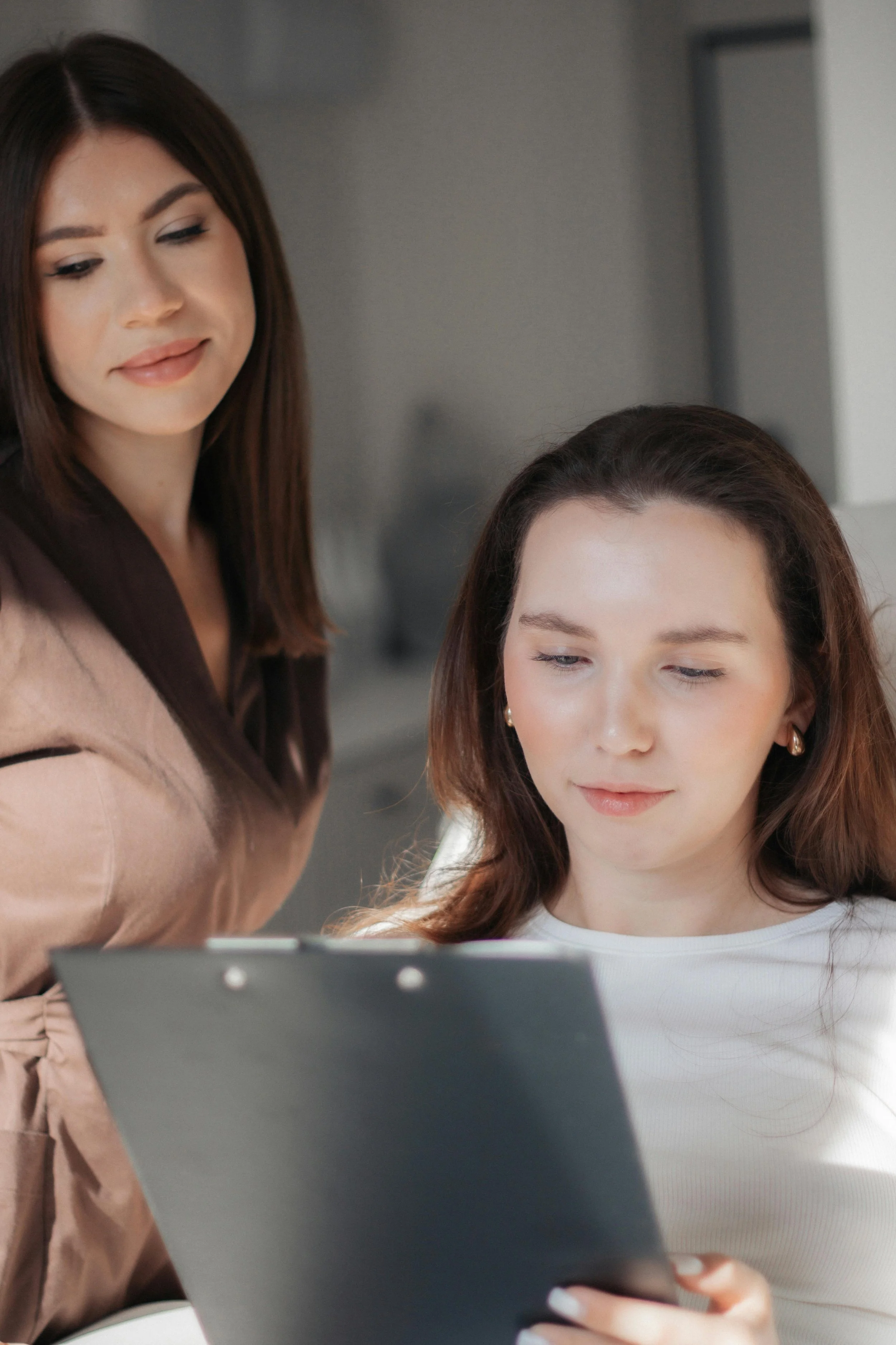 Two women looking at a tablet, one standing behind the other.