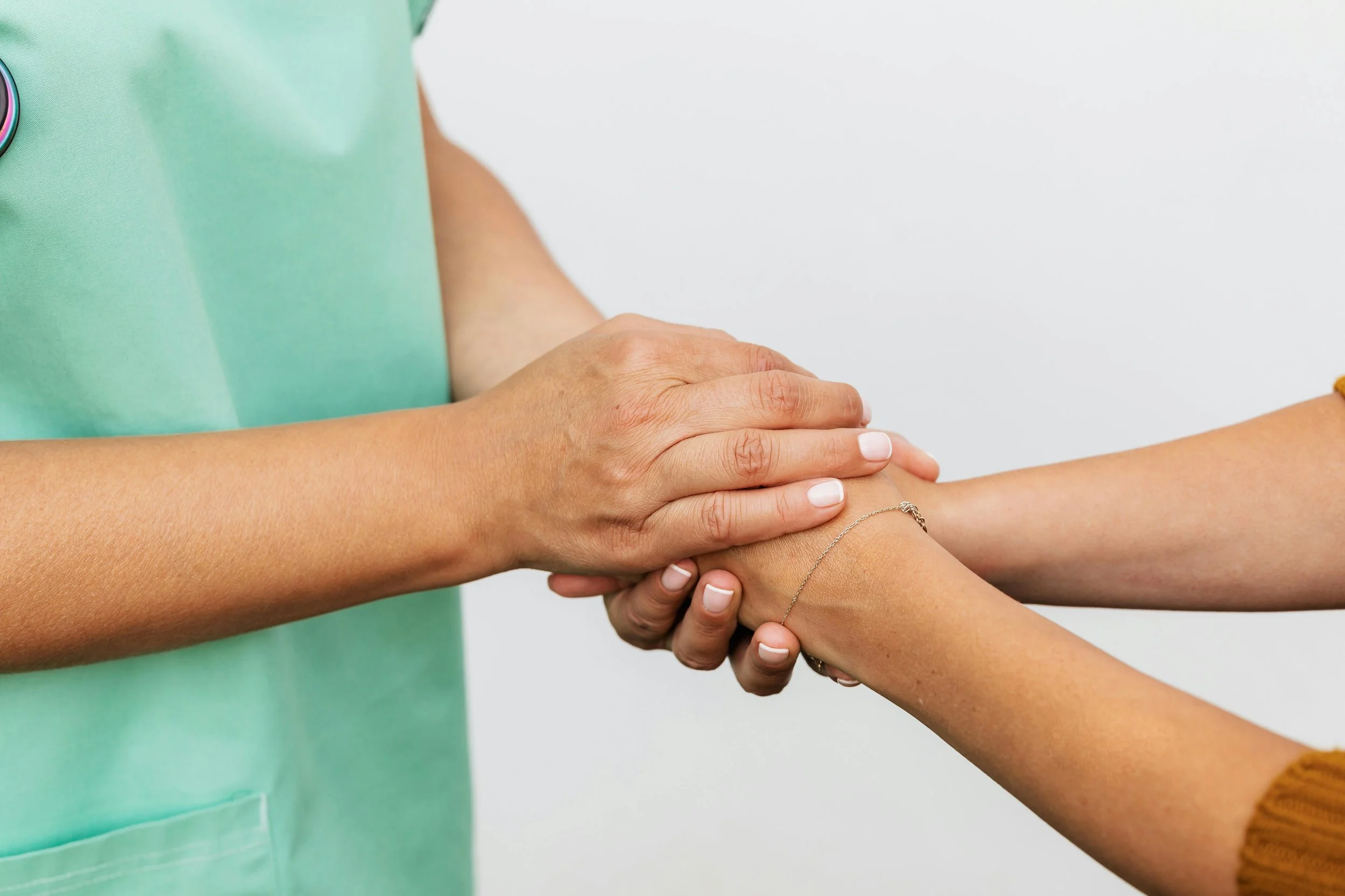 A healthcare professional in a green uniform gently holds a patient's arm, indicating a medical or caring context.