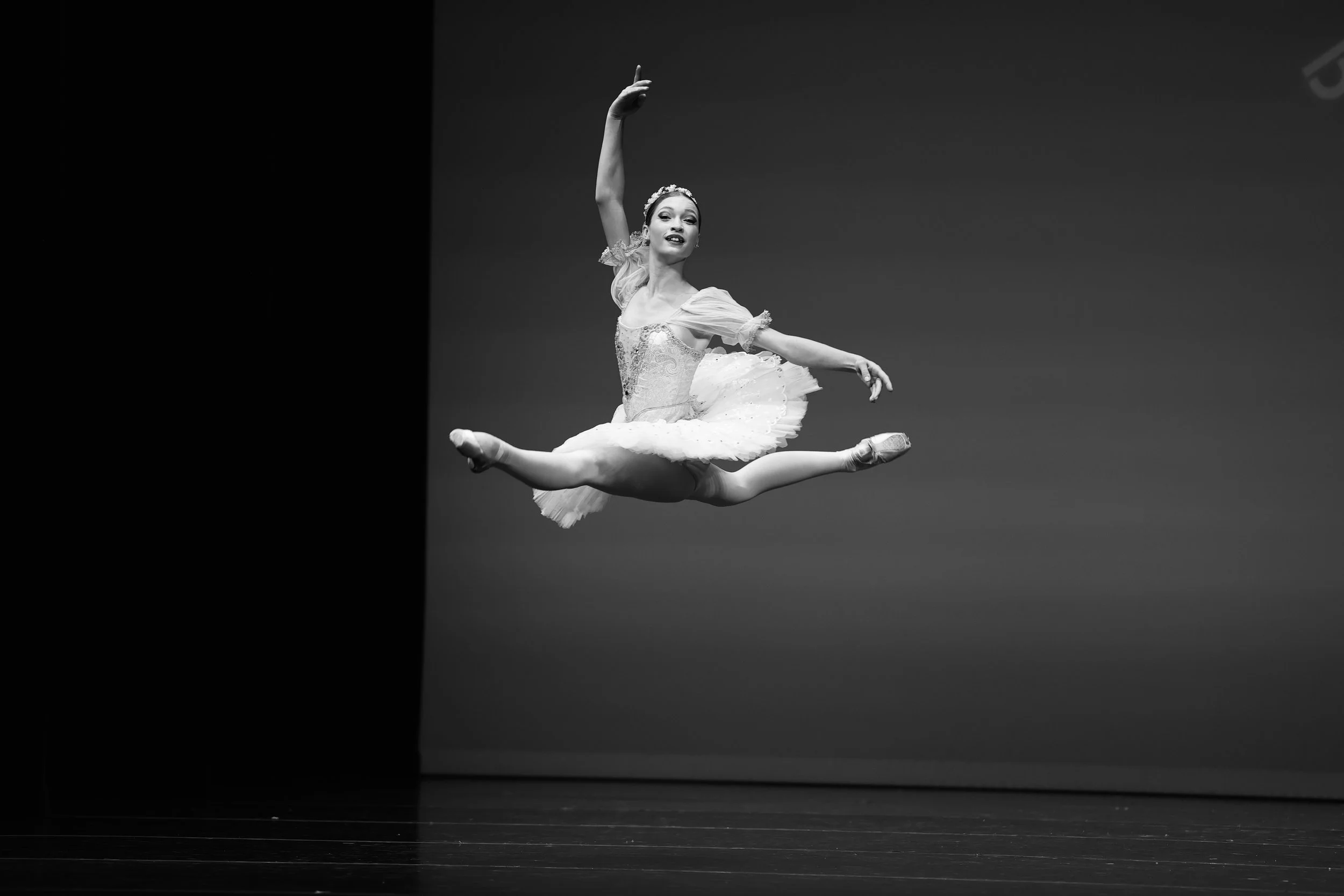 A ballerina performing a leap on stage, wearing a tutu and pointe shoes, dancing Coppelia, captured in black and white.