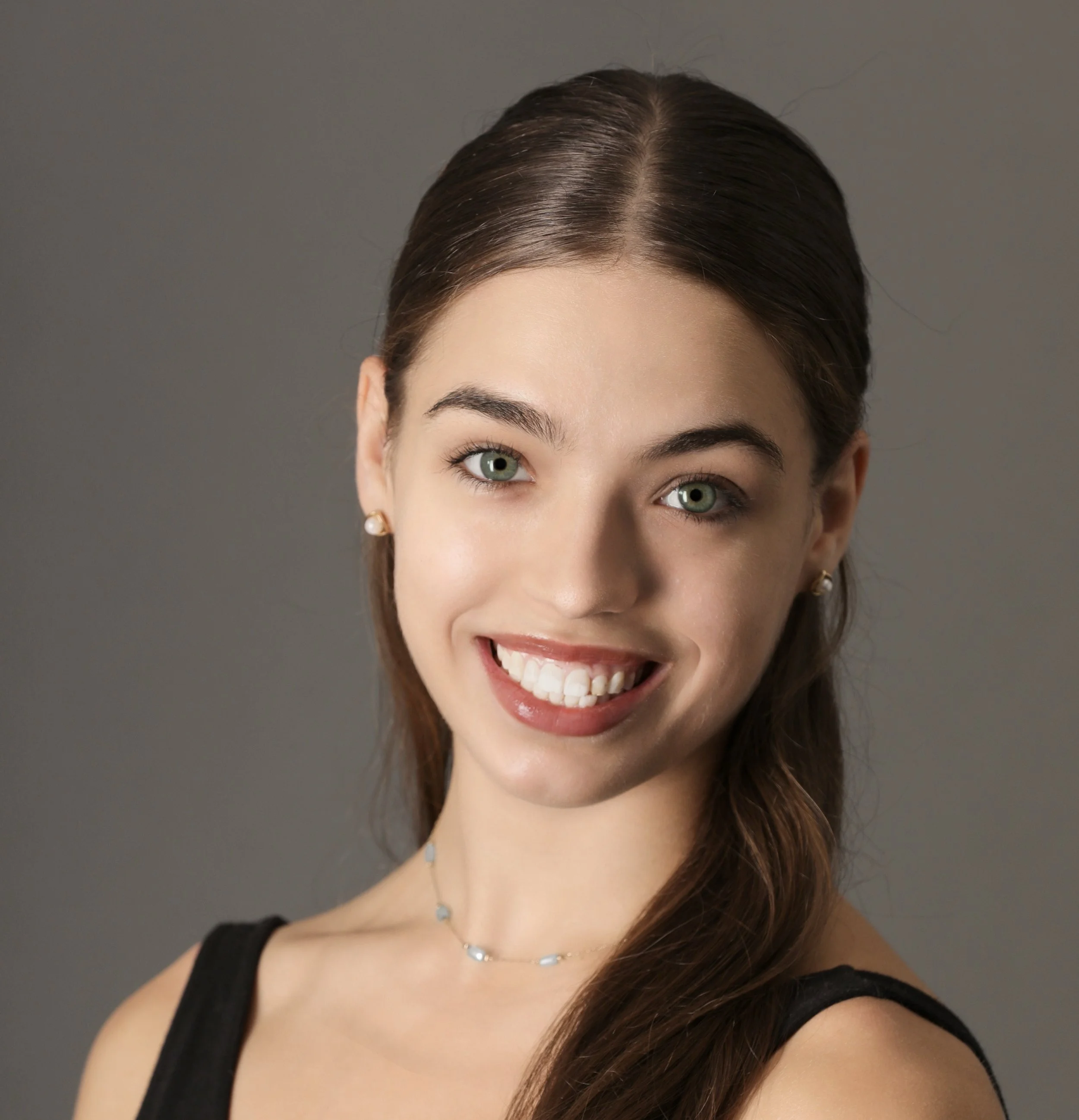 A young woman with long brown hair, wearing a black sleeveless top, pearl earrings, and a delicate necklace, smiling against a plain gray background.