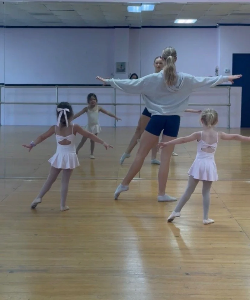 Ballet dancer in practice attire, standing in front of mirror at ballet barre in dance studio.